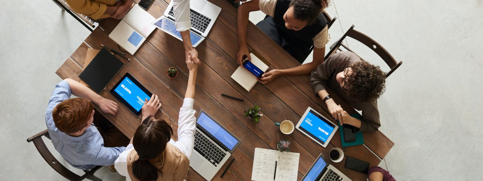 Équipe de travail se saluant dans une réunion avec ordinateurs portables et tablettes sur la table.