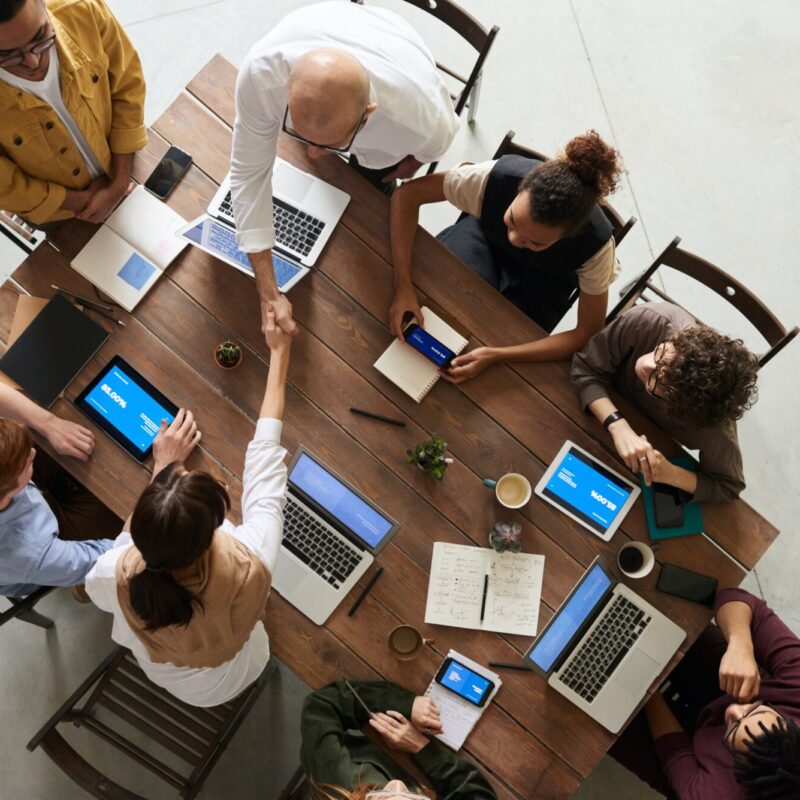 Équipe de travail se saluant dans une réunion avec ordinateurs portables et tablettes sur la table.