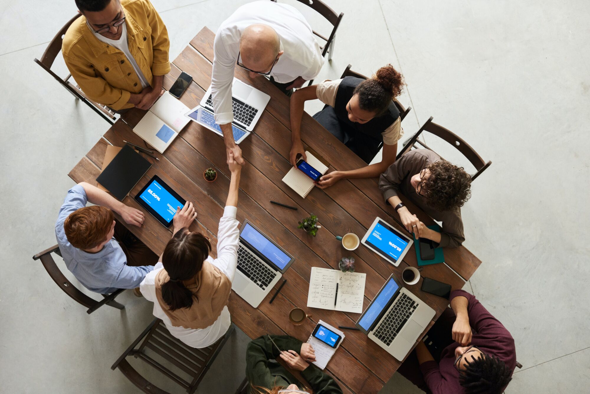 Équipe de travail se saluant dans une réunion avec ordinateurs portables et tablettes sur la table.