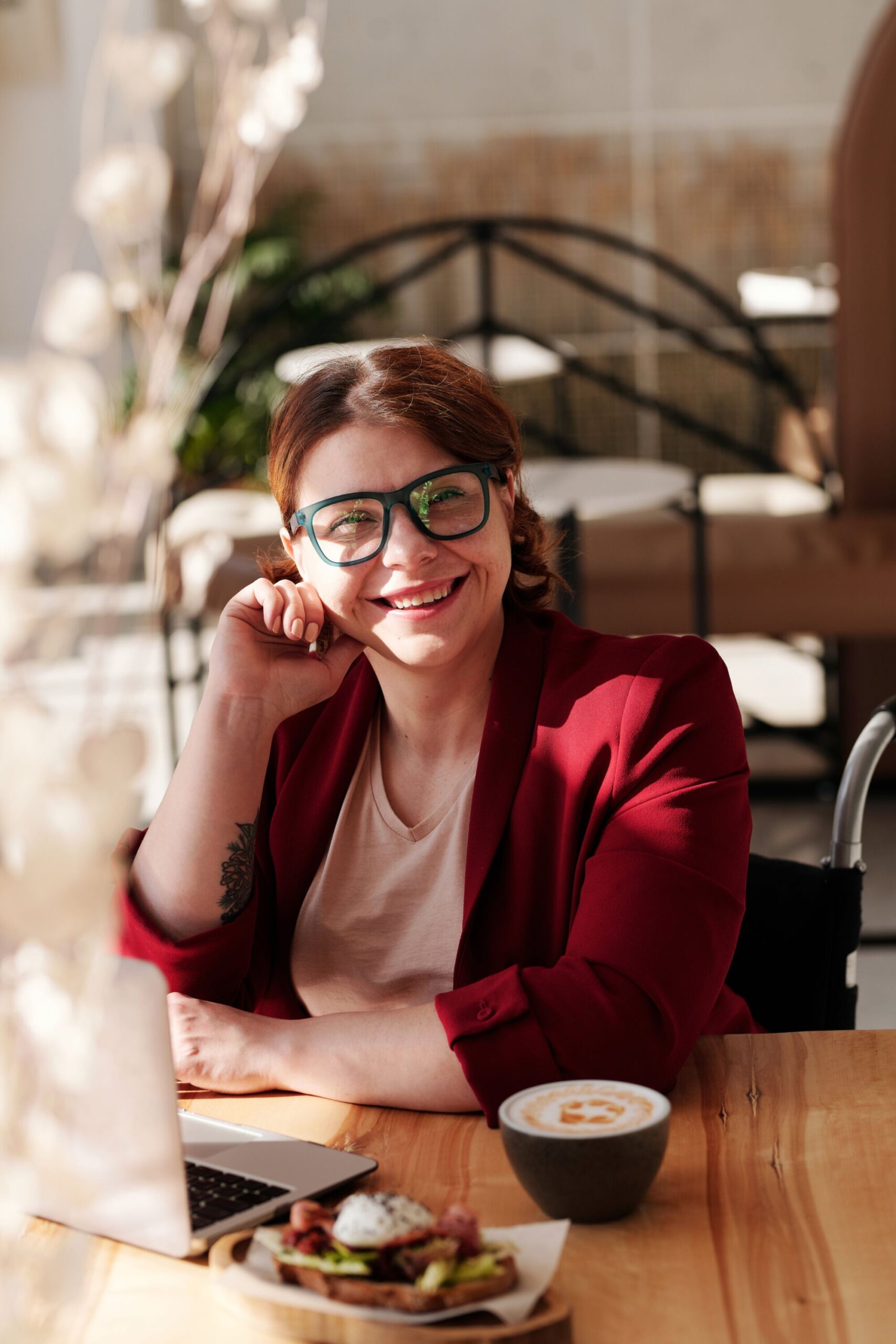 Femme en tenue décontractée professionnelle souriante et travaillant sur un ordinateur portable dans un espace de café.