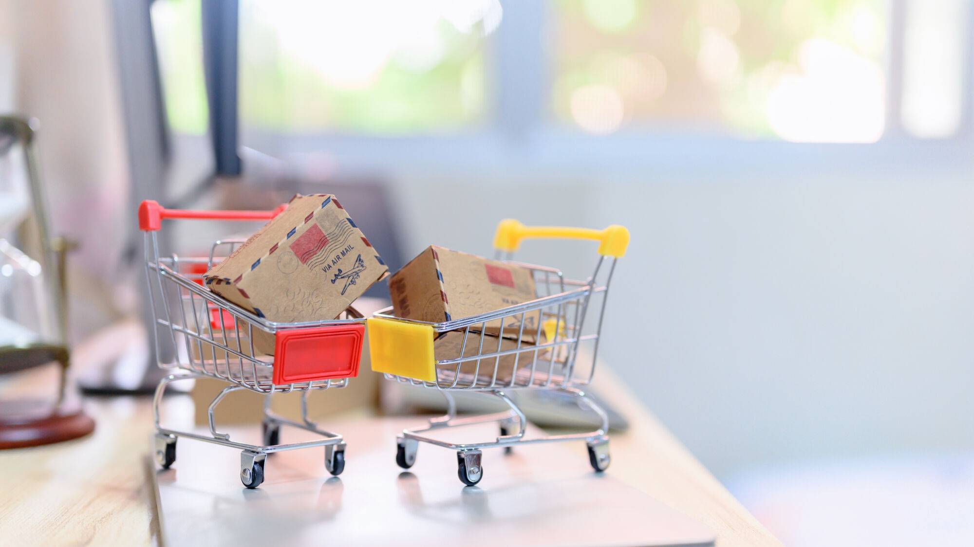 Mini caddie de supermarché contenant des paquets sur un bureau, symbolisant les achats en ligne.