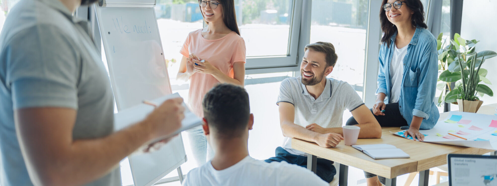 Groupe de collègues souriants participant à une présentation avec un tableau blanc dans un bureau lumineux.