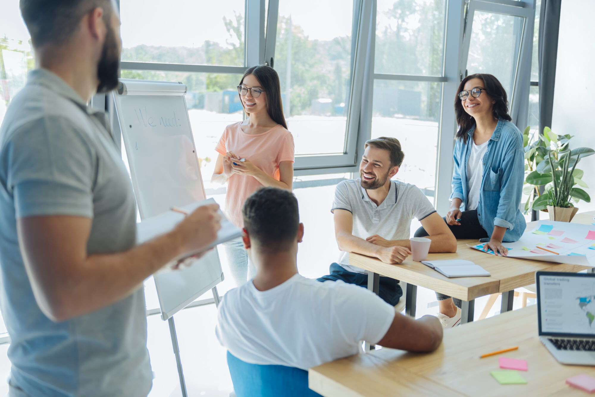 Groupe de collègues souriants participant à une présentation avec un tableau blanc dans un bureau lumineux.