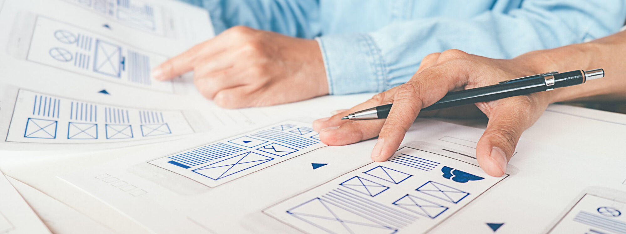 Gros plan sur les mains d'une personne analysant des maquettes de conception d'interface utilisateur.