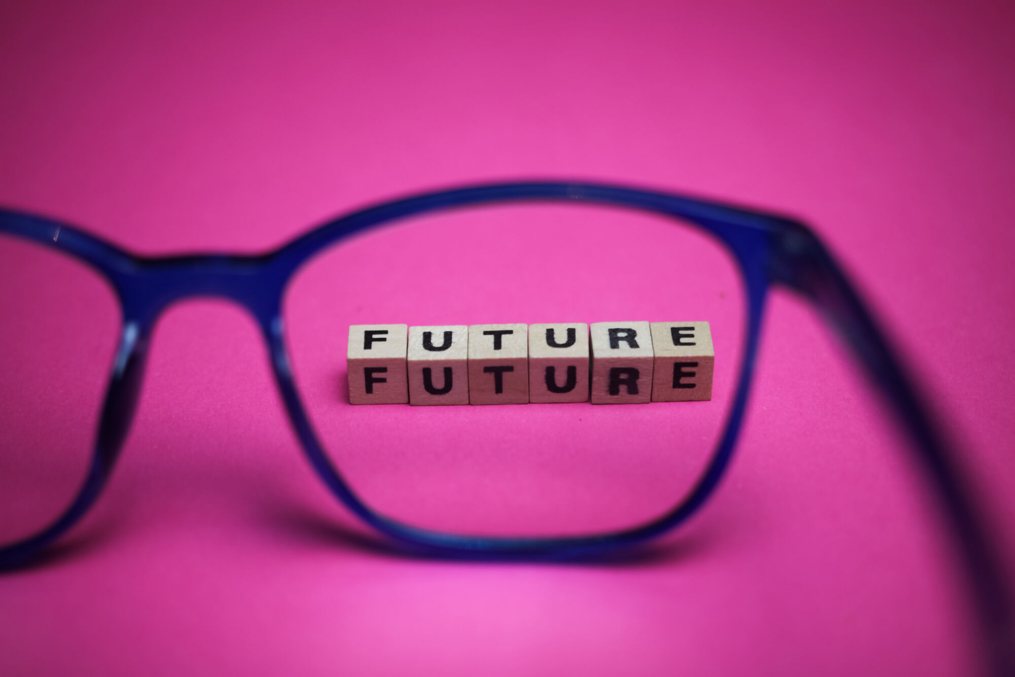 Lunettes bleues mettant en évidence des cubes en bois formant le mot 'FUTURE' sur un fond rose.