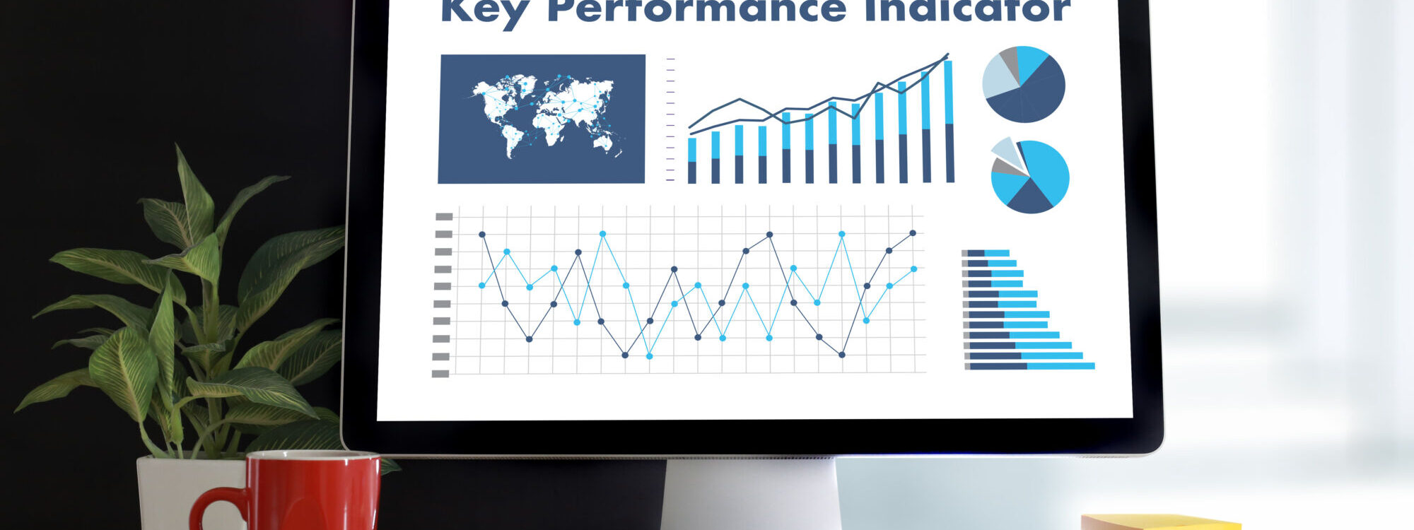 Écran d'ordinateur montrant des graphiques et des données pour les indicateurs de performance clés (KPI) avec une plante et une tasse rouge sur le bureau.