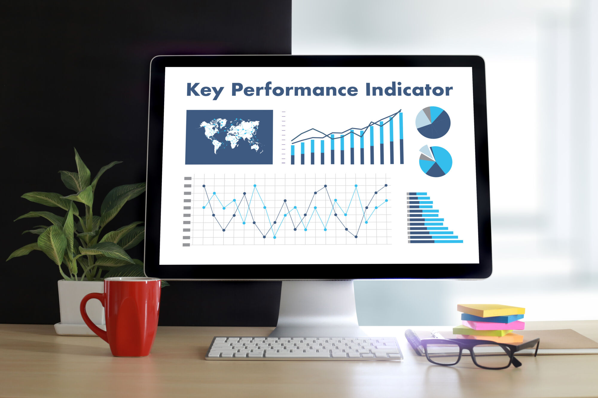 Écran d'ordinateur montrant des graphiques et des données pour les indicateurs de performance clés (KPI) avec une plante et une tasse rouge sur le bureau.