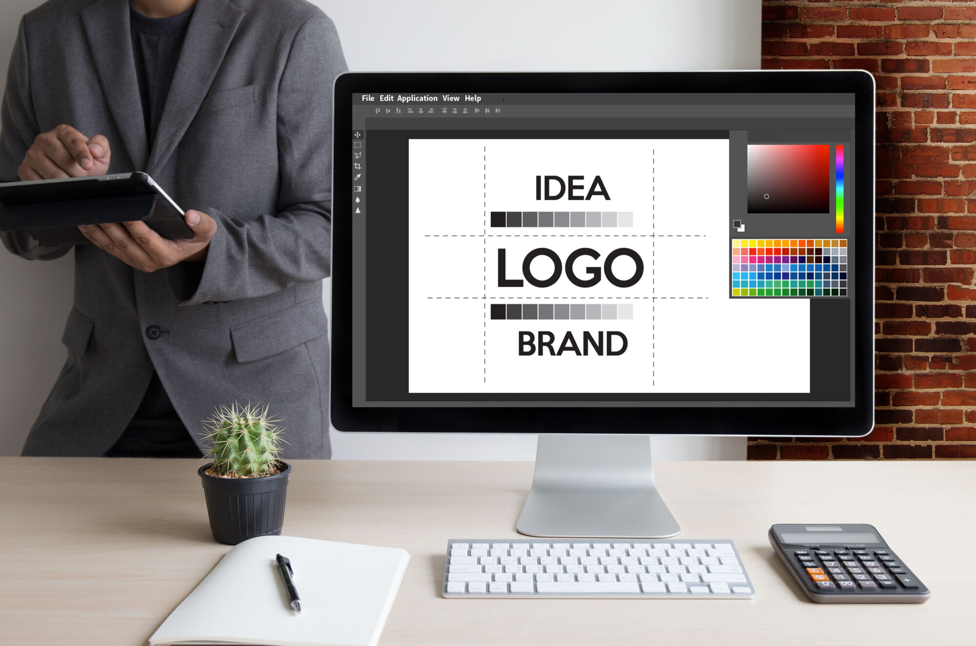 Écran d'ordinateur affichant un logiciel de conception graphique avec des mots 'IDEA', 'LOGO', 'BRAND' sur le moniteur.