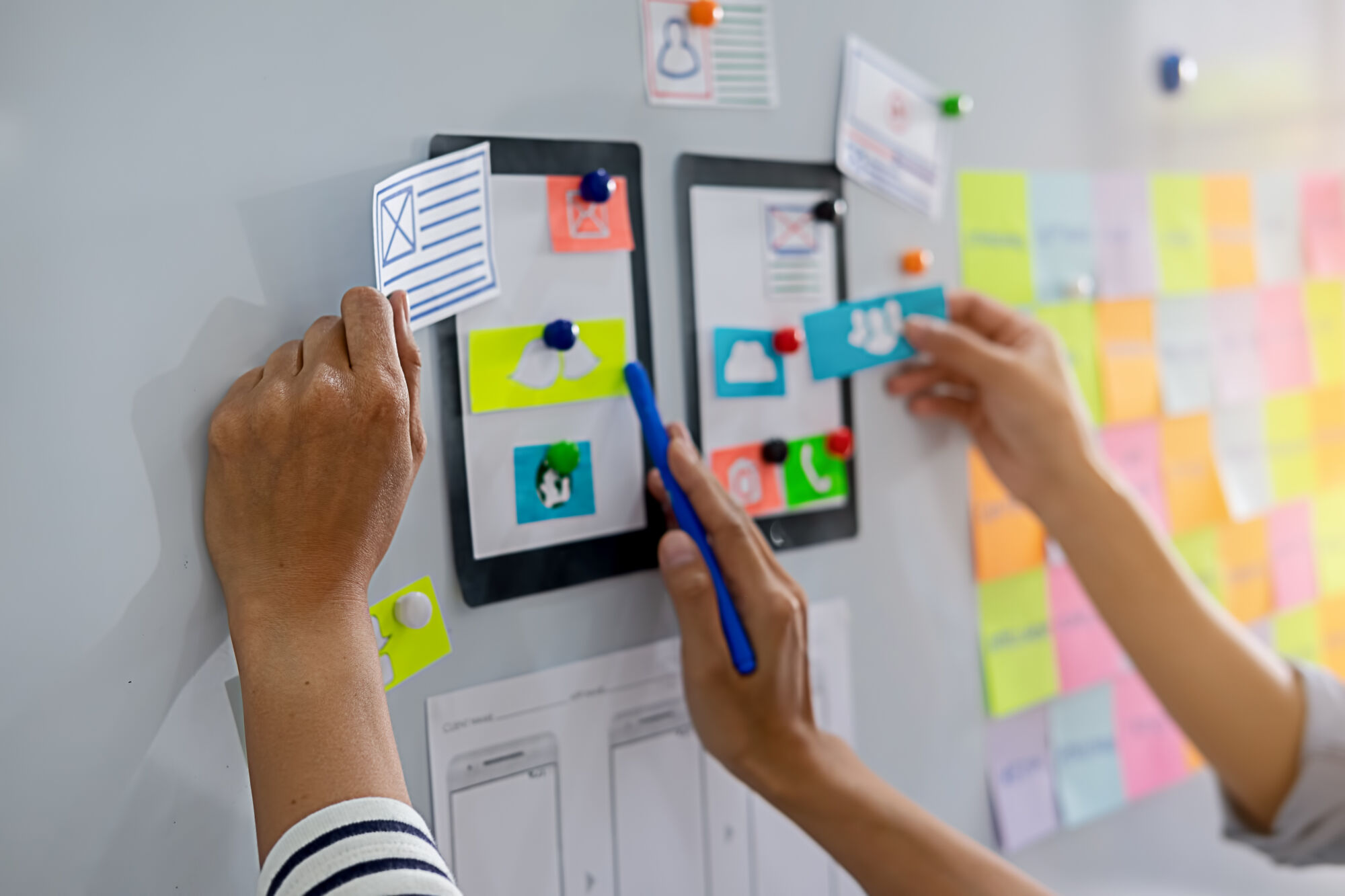 Mains plaçant des notes adhésives et des icônes sur un tableau blanc lors d'une séance de brainstorming pour le développement d'applications.