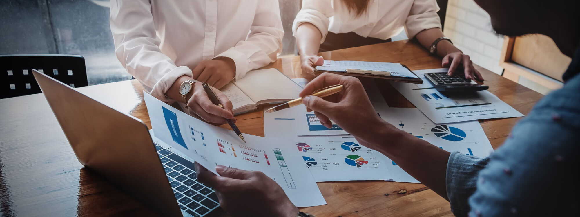 Équipe discutant des analyses financières et des stratégies marketing avec des graphiques et des ordinateurs portables sur une table en bois.