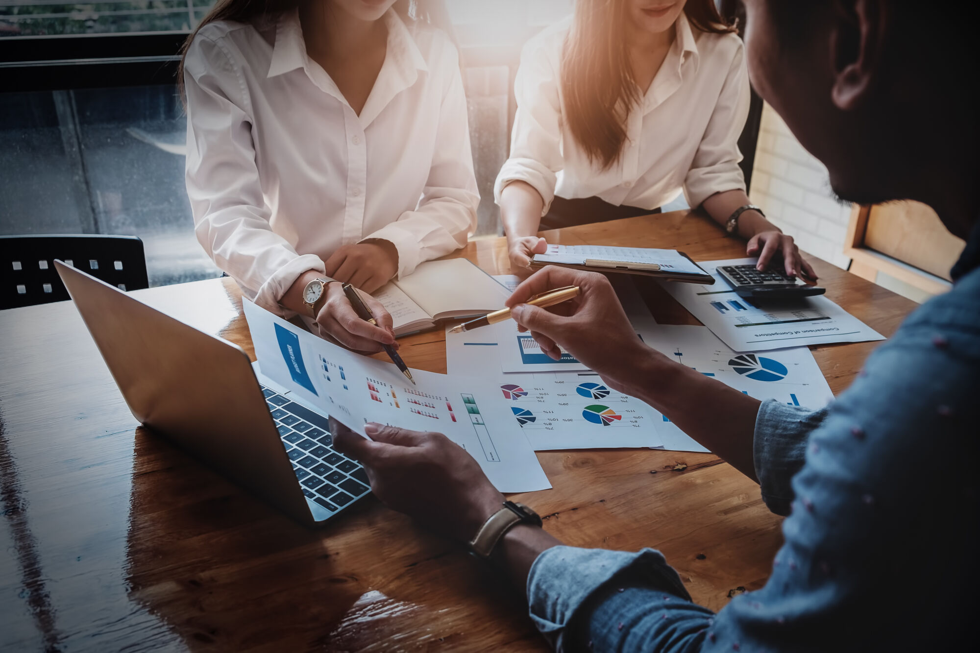 Équipe discutant des analyses financières et des stratégies marketing avec des graphiques et des ordinateurs portables sur une table en bois.