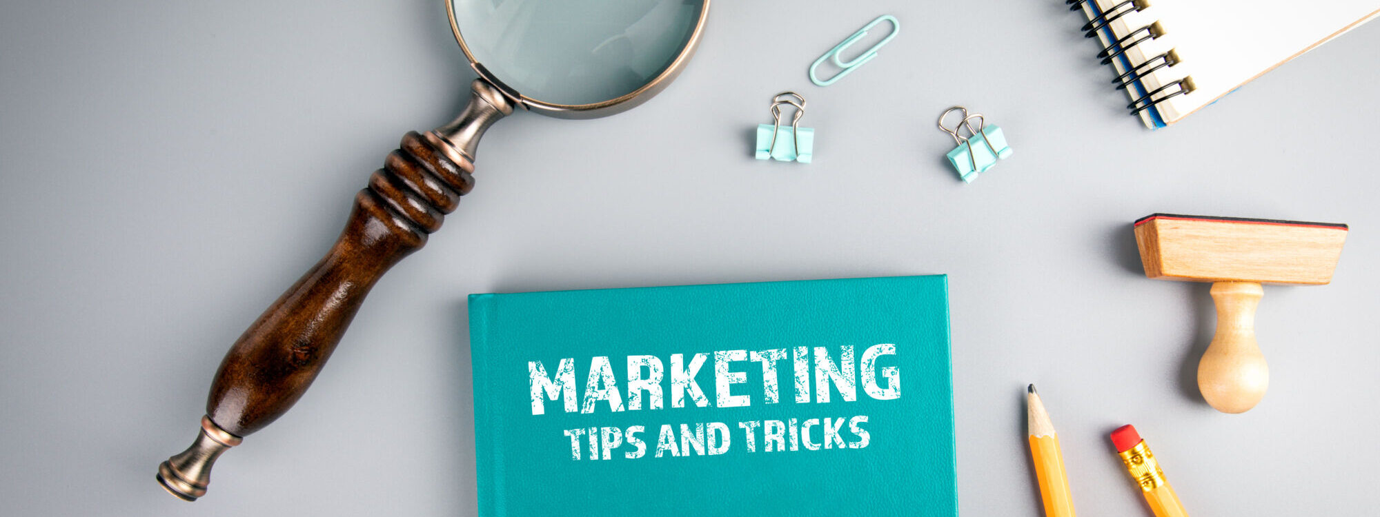 Bureau avec un cahier indiquant 'MARKETING TIPS AND TRICKS', une loupe et des fournitures de bureau.