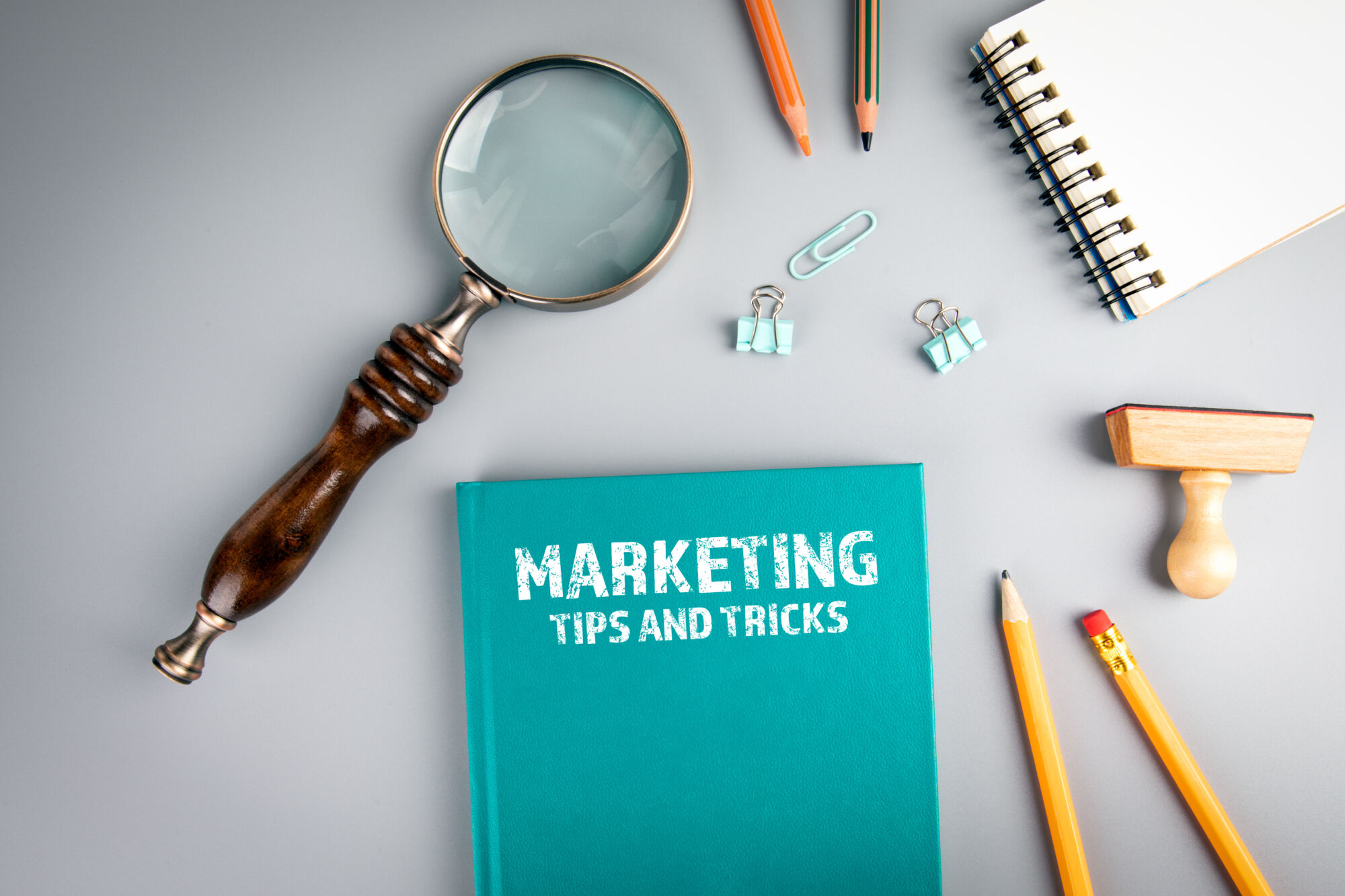 Bureau avec un cahier indiquant 'MARKETING TIPS AND TRICKS', une loupe et des fournitures de bureau.