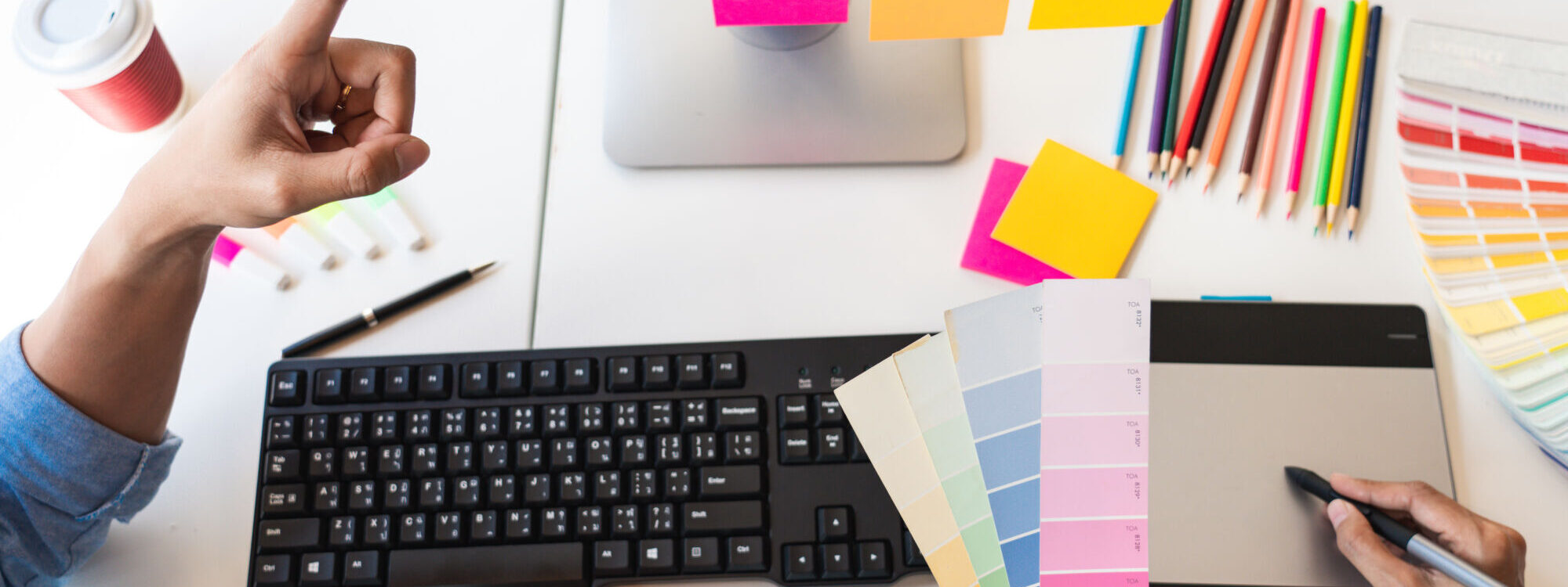 Bureau de conception graphique avec échantillons de palettes de couleurs et notes adhésives sur un moniteur.