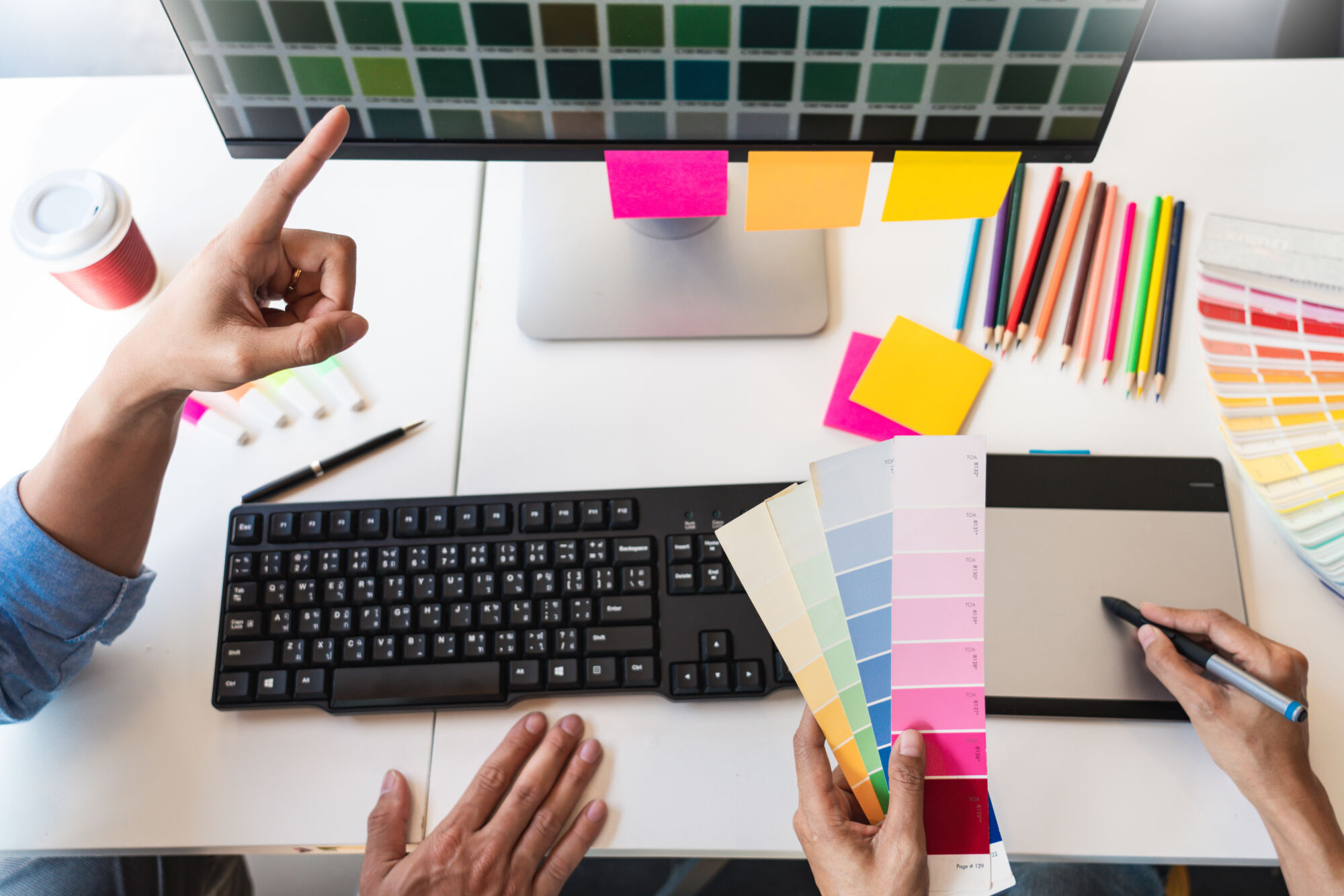 Bureau de conception graphique avec échantillons de palettes de couleurs et notes adhésives sur un moniteur.