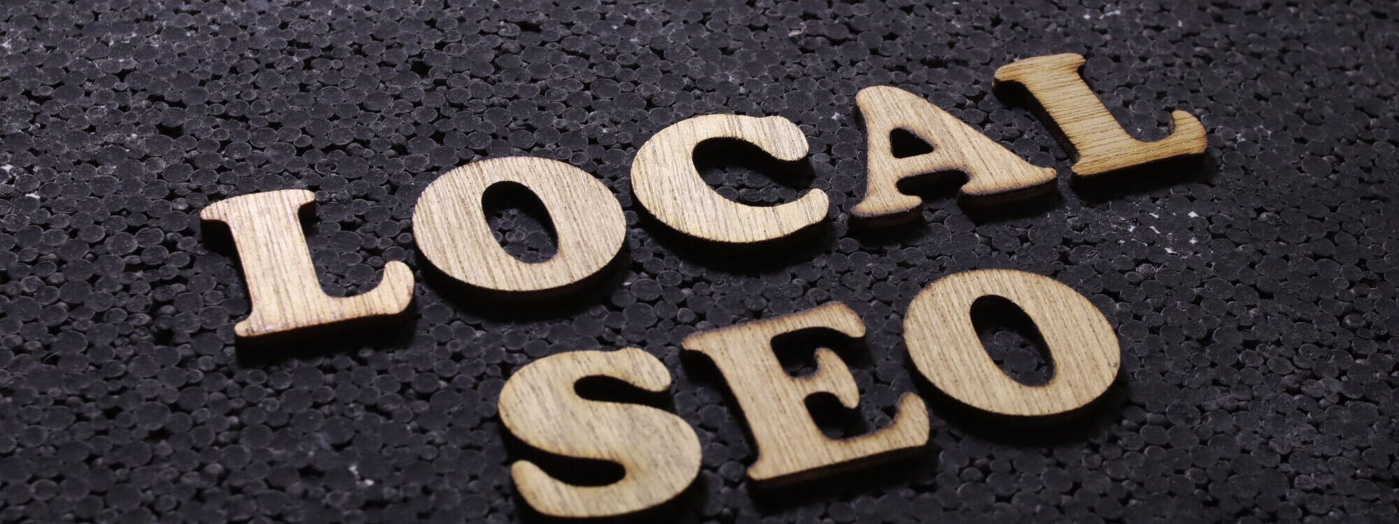 Le terme 'LOCAL SEO' en lettres en bois sur un fond texturé noir, concept de référencement local.