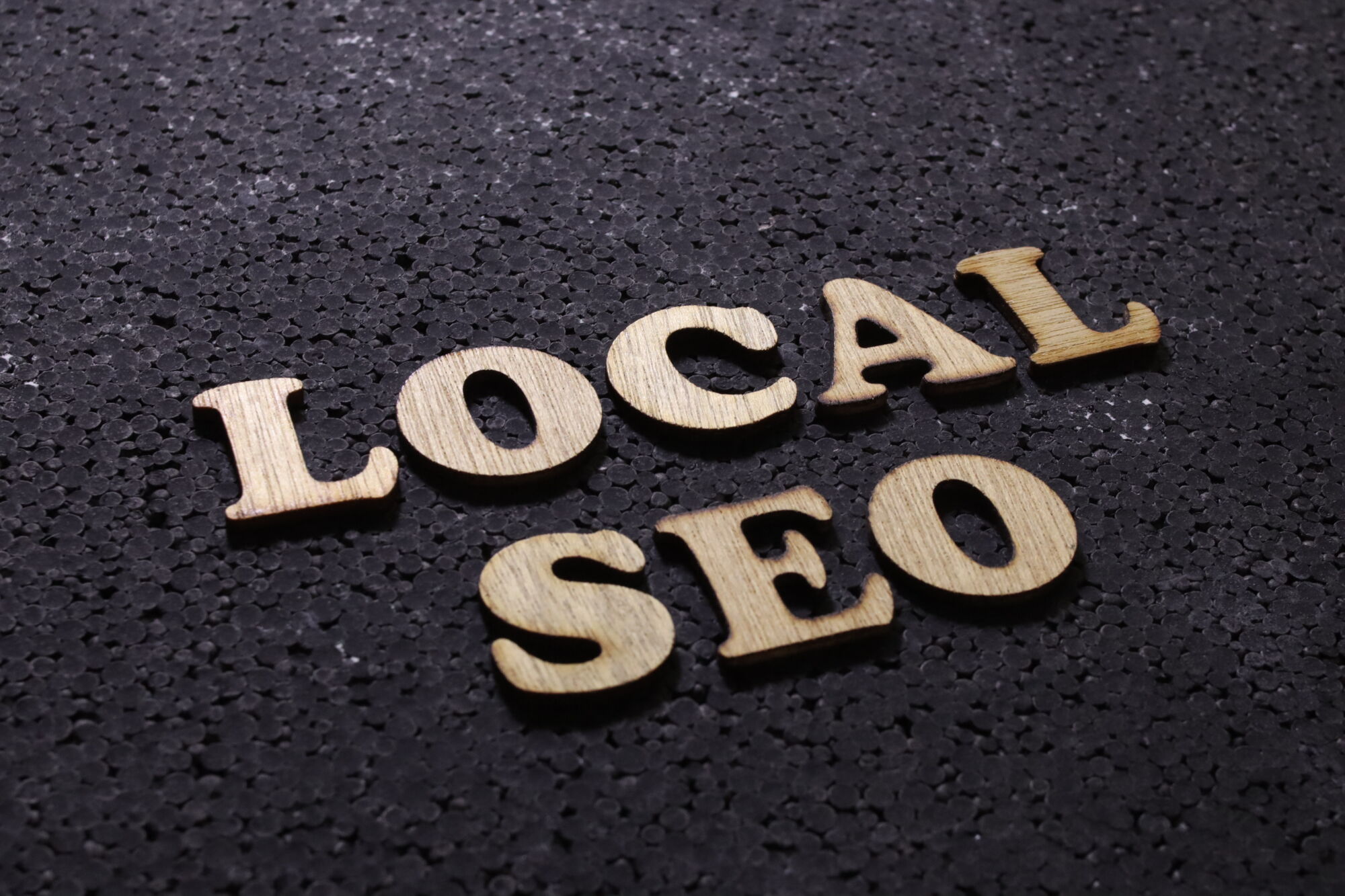 Le terme 'LOCAL SEO' en lettres en bois sur un fond texturé noir, concept de référencement local.