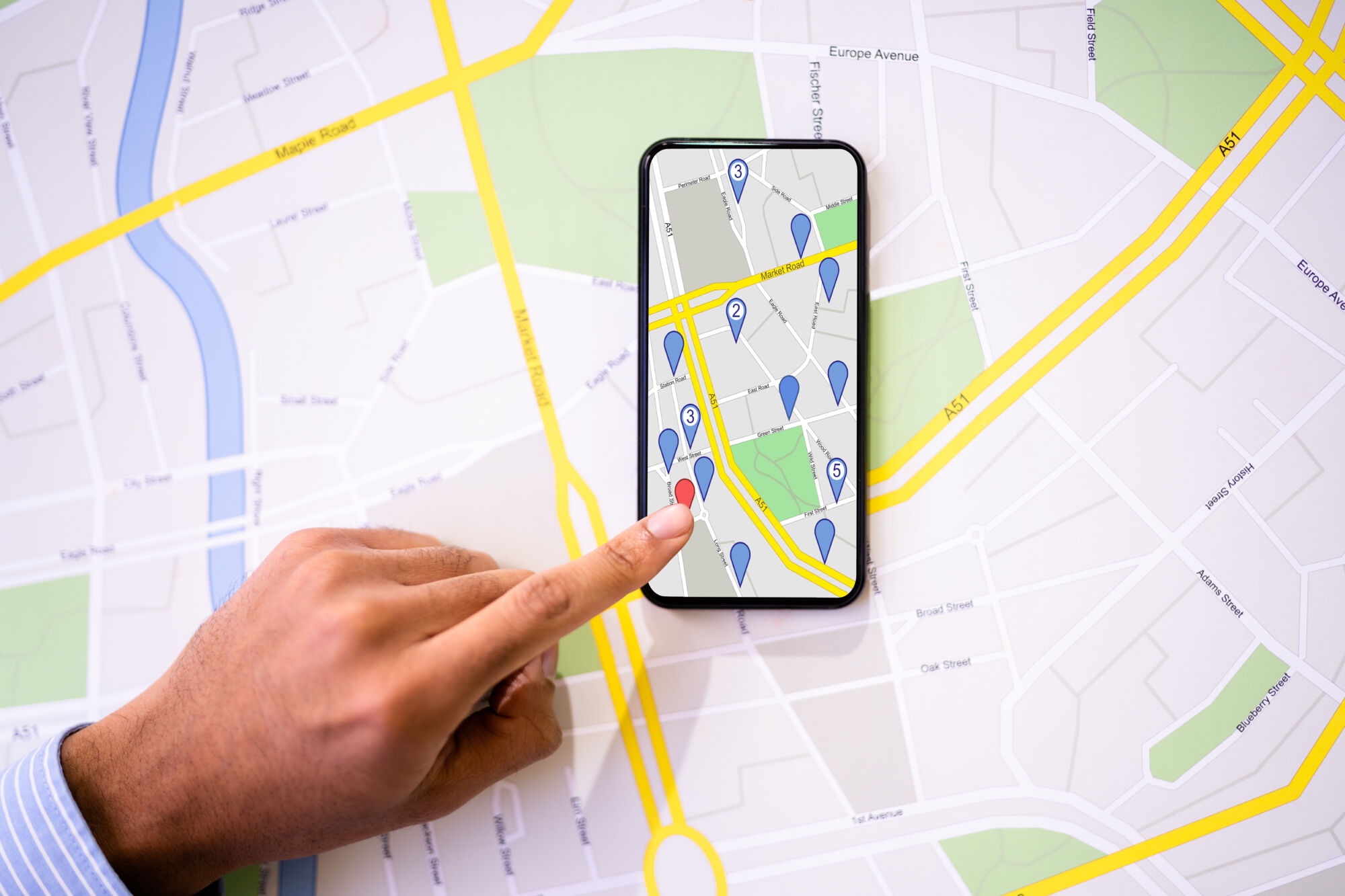Doigt pointant sur une carte interactive sur un smartphone avec des icônes de localisation et un plan de ville en arrière-plan.