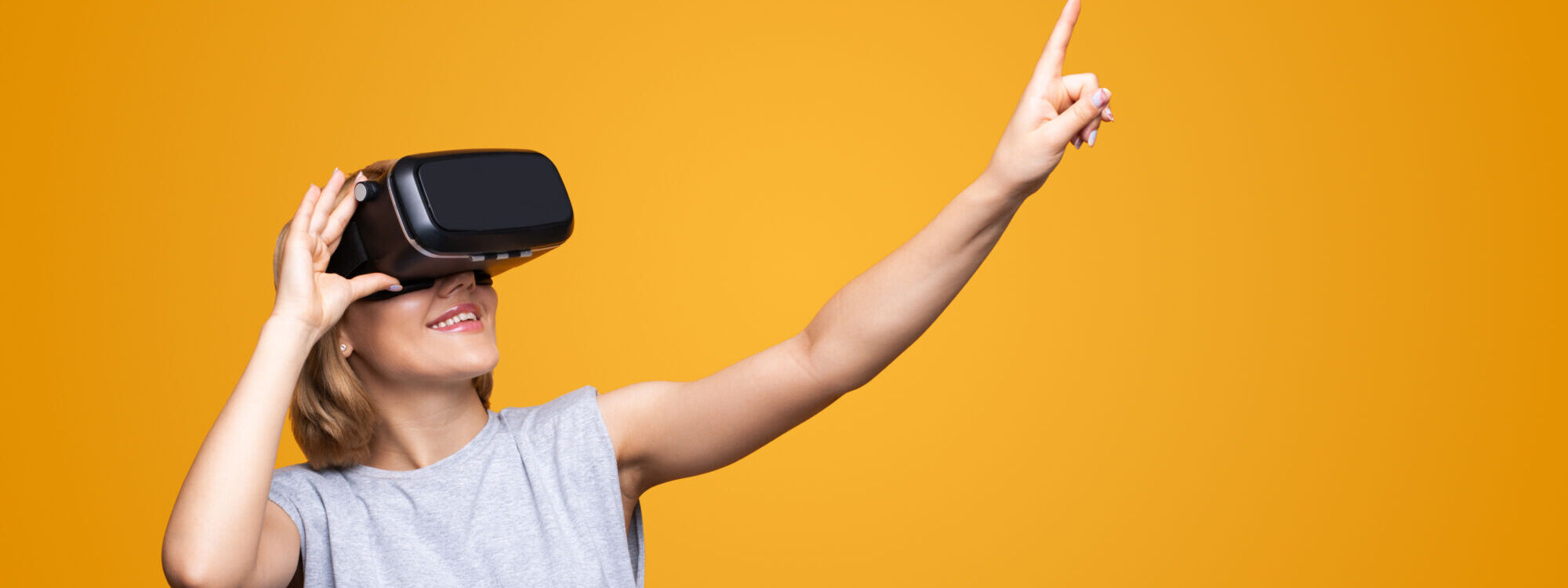 Femme souriante utilisant un casque de réalité virtuelle pointant vers un espace vide sur fond orange