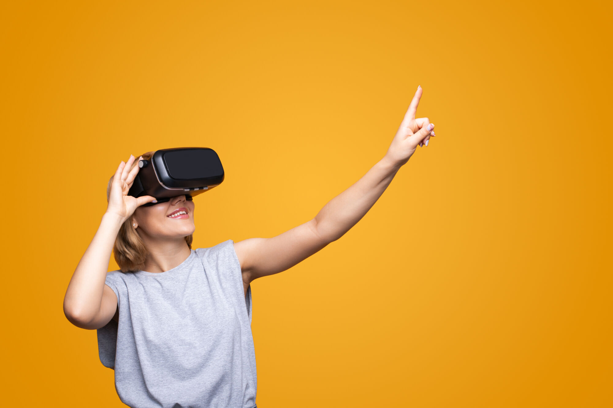 Femme souriante utilisant un casque de réalité virtuelle pointant vers un espace vide sur fond orange