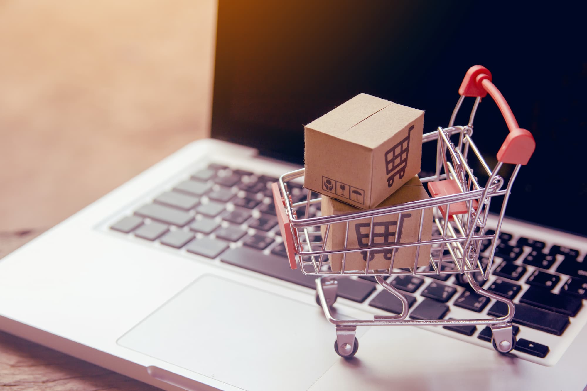 Mini caddie sur un clavier d'ordinateur avec une boîte en carton, évoquant l'achat en ligne ou l'e-commerce.