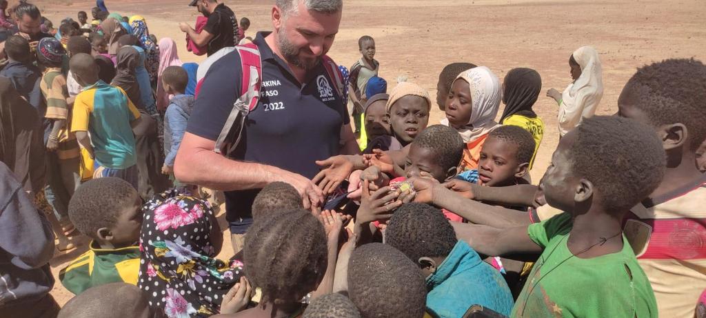 Homme partageant un moment avec des enfants enthousiastes lors d'une distribution en plein air.