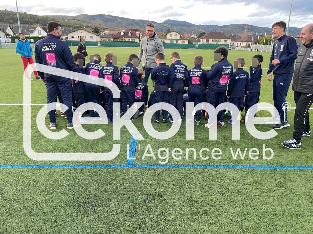 Équipe de jeunes footballeurs écoutant leur entraîneur sur un terrain de sport.