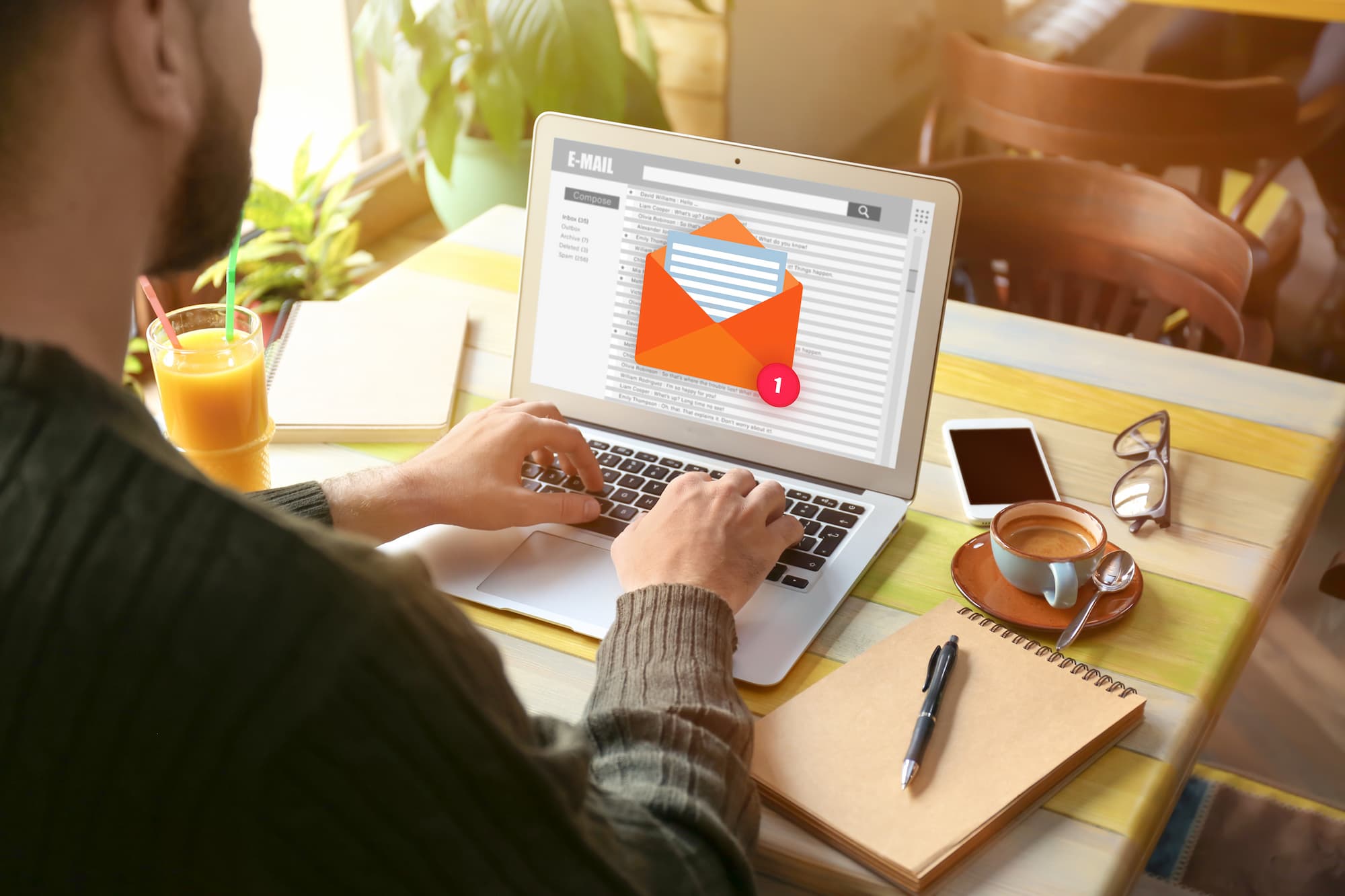 Homme utilisant un ordinateur portable avec notification d'email à l'écran, verre de jus et café sur la table.