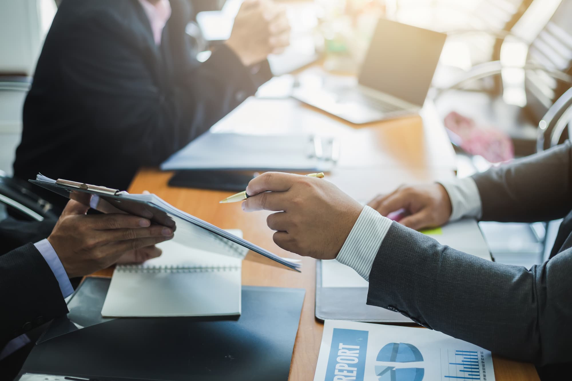 Deux professionnels en réunion avec ordinateur portable et documents financiers sur la table.