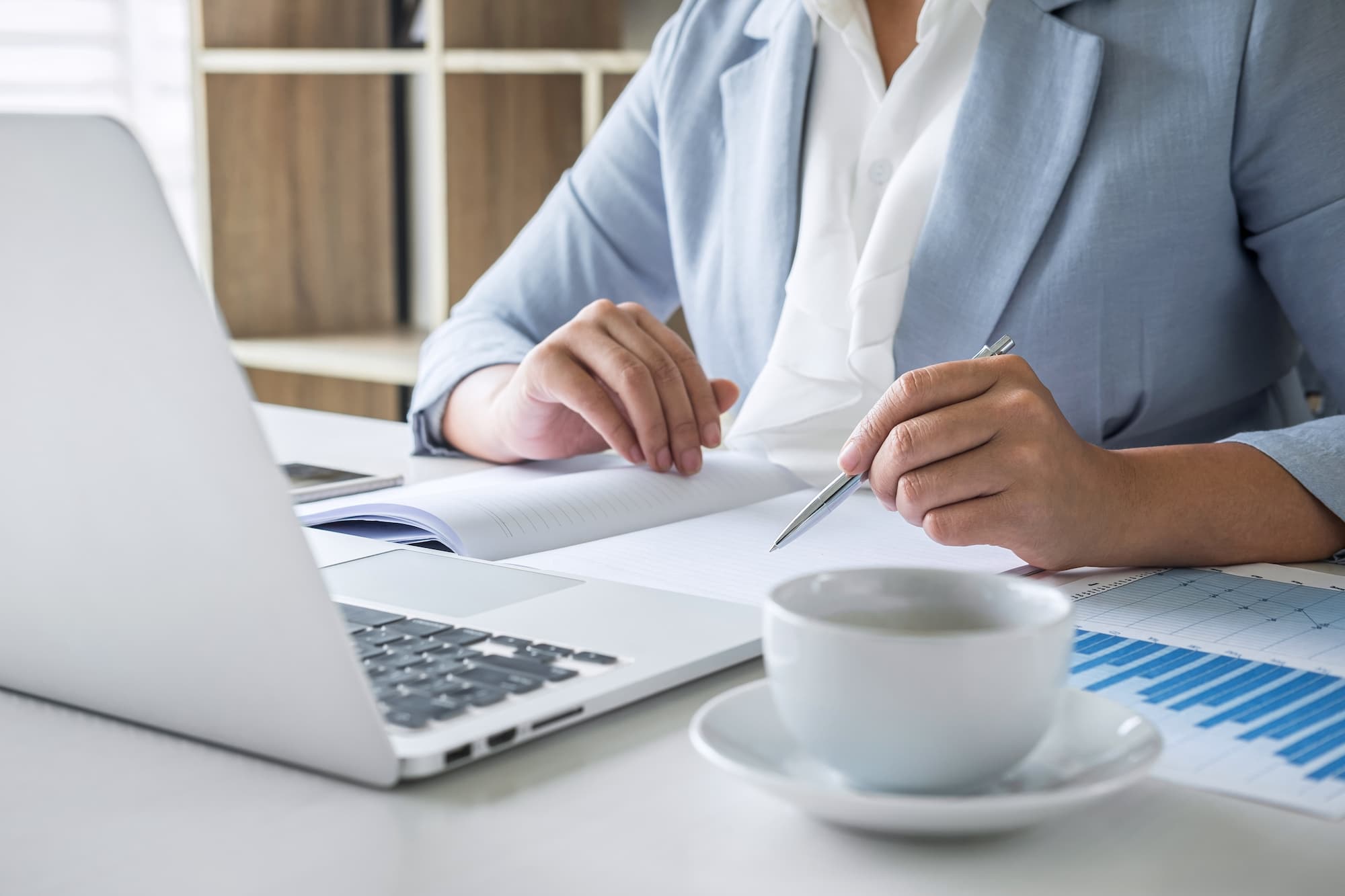 Professionnelle en finance consultant des documents et travaillant sur ordinateur portable avec une tasse de café.