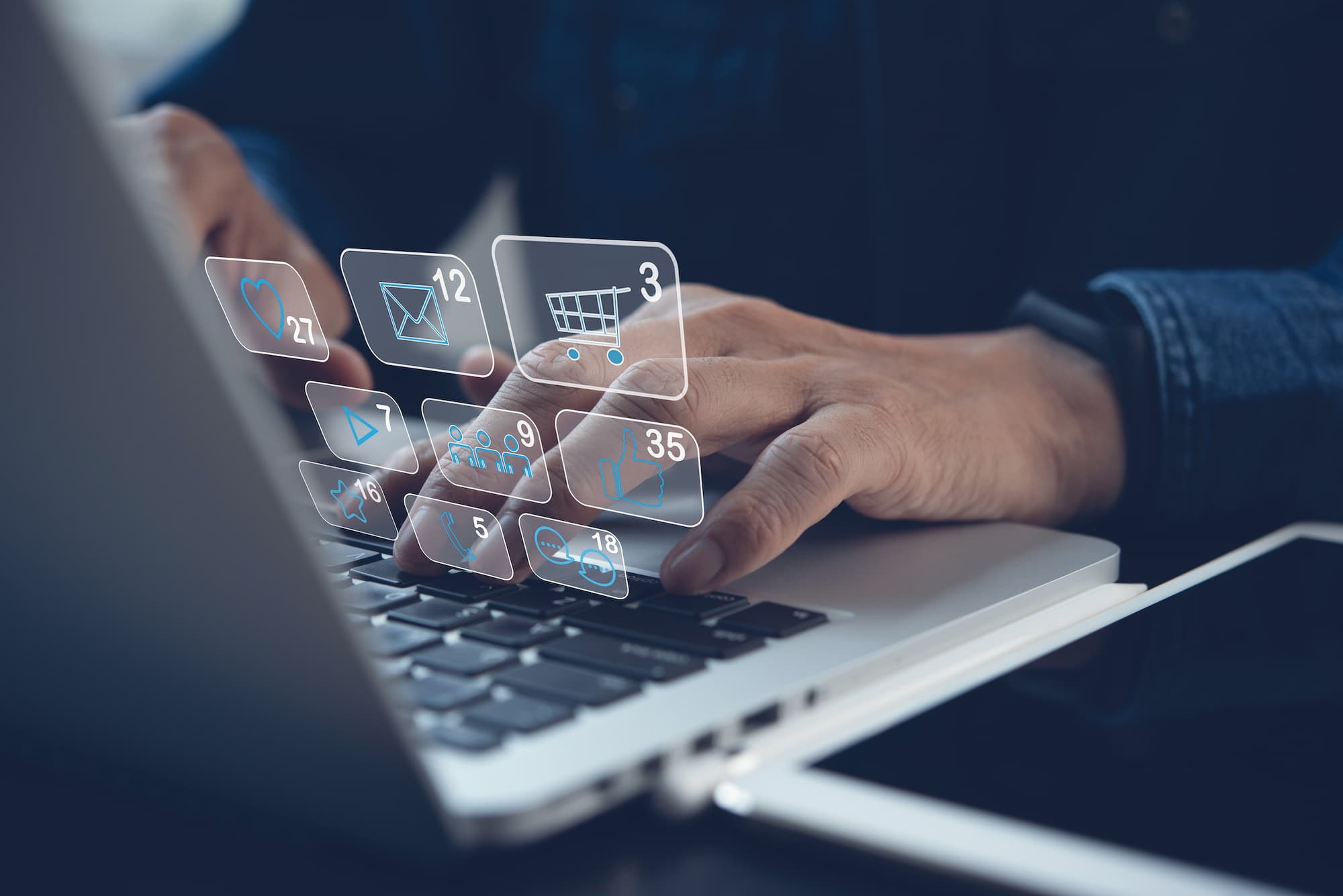 Main utilisant un ordinateur portable avec des icônes flottantes de notifications de médias sociaux, de panier d'achat et de messagerie.