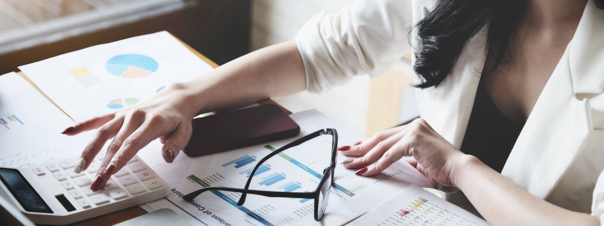 Femme d'affaires calculant des statistiques financières avec des graphiques et un ordinateur portable.