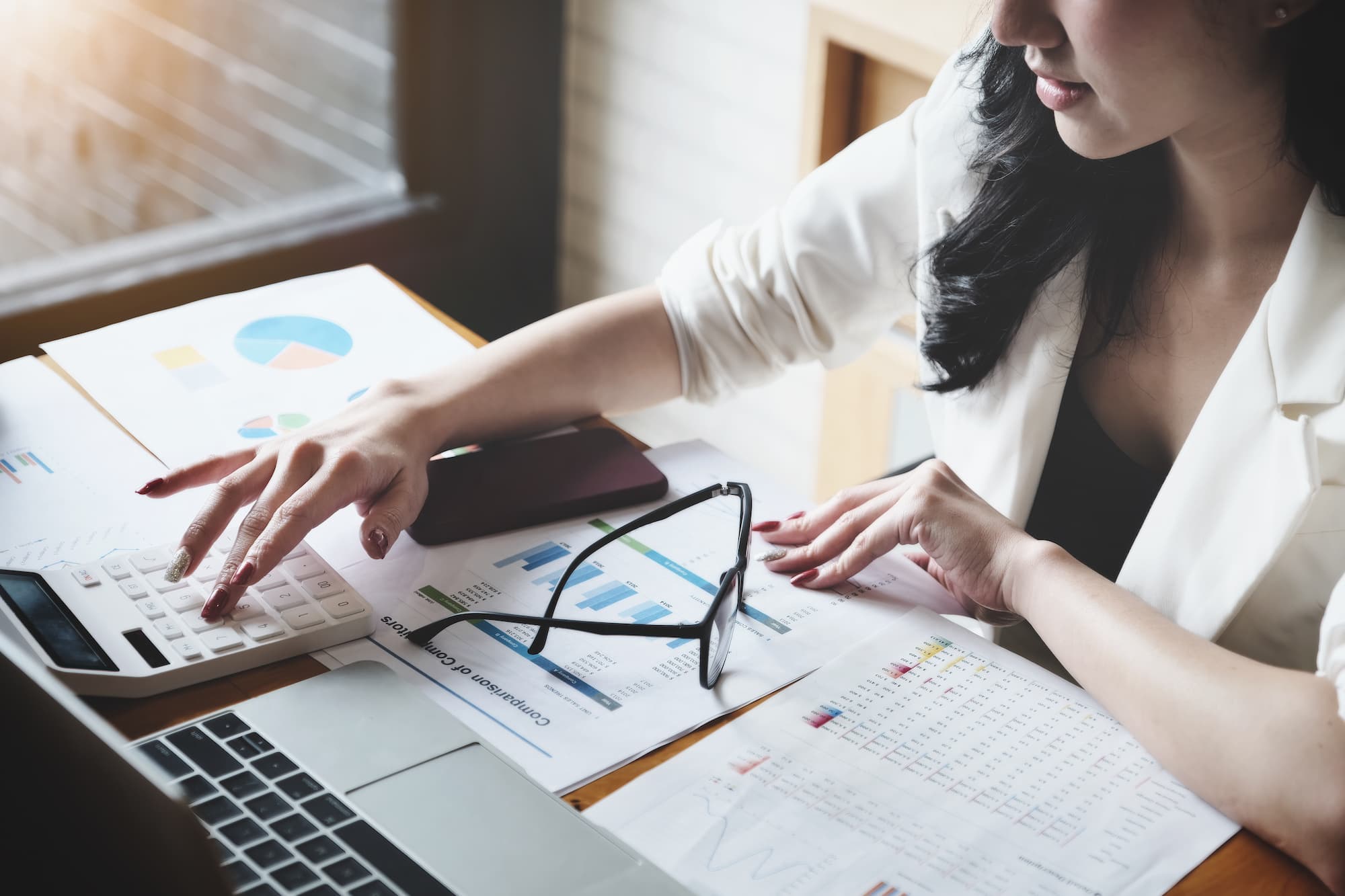 Femme d'affaires calculant des statistiques financières avec des graphiques et un ordinateur portable.