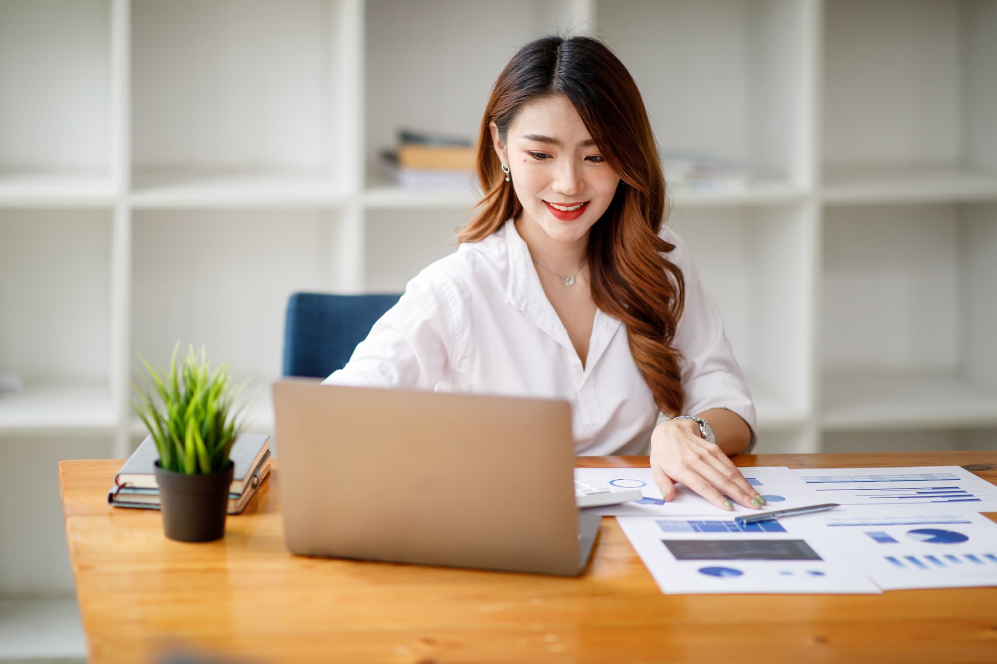 Jeune femme entrepreneur examinant des rapports financiers sur son bureau avec ordinateur portable ouvert.