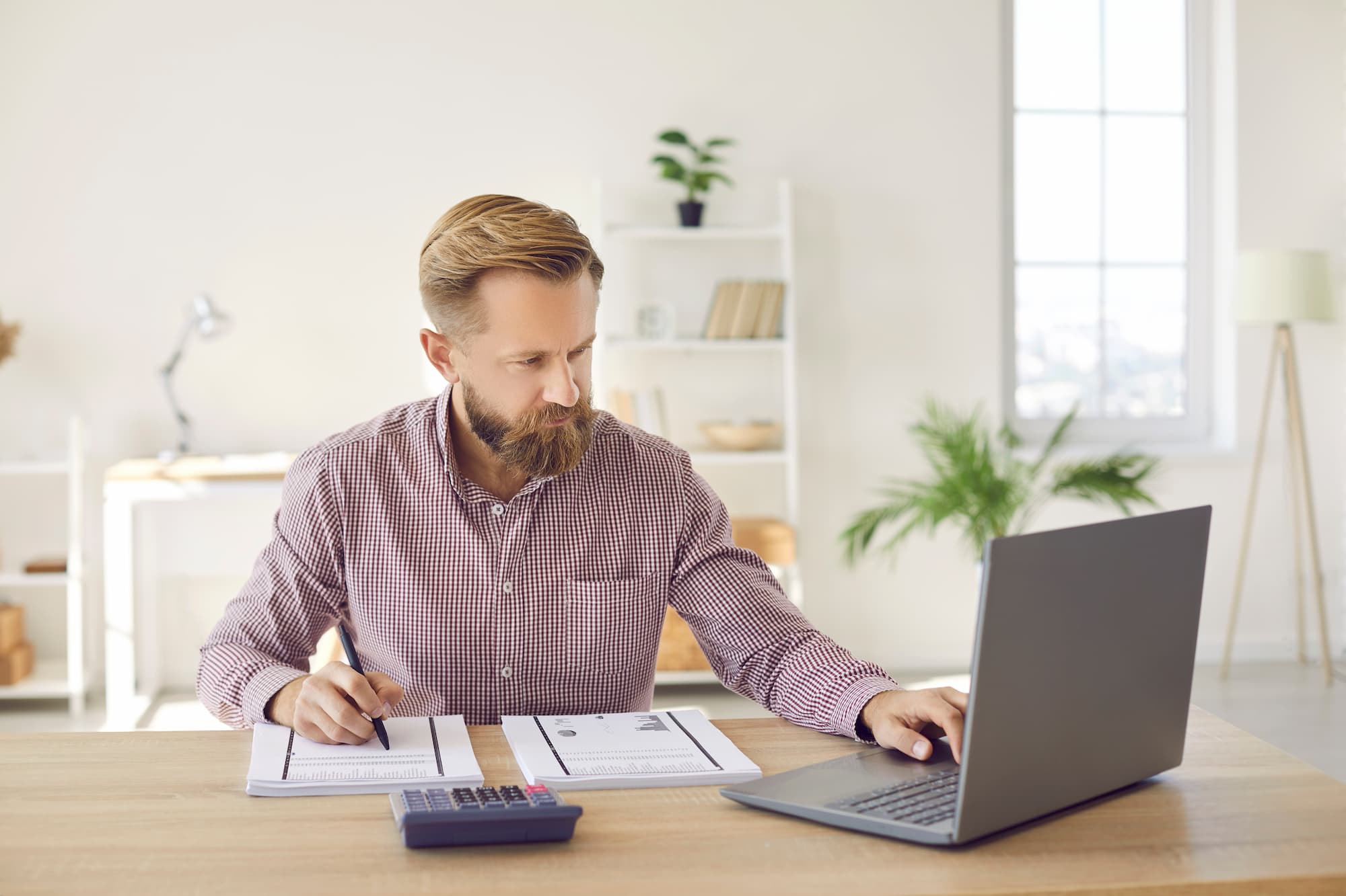 Homme d'affaires concentré travaillant sur ordinateur portable avec documents comptables et calculatrice sur son bureau.