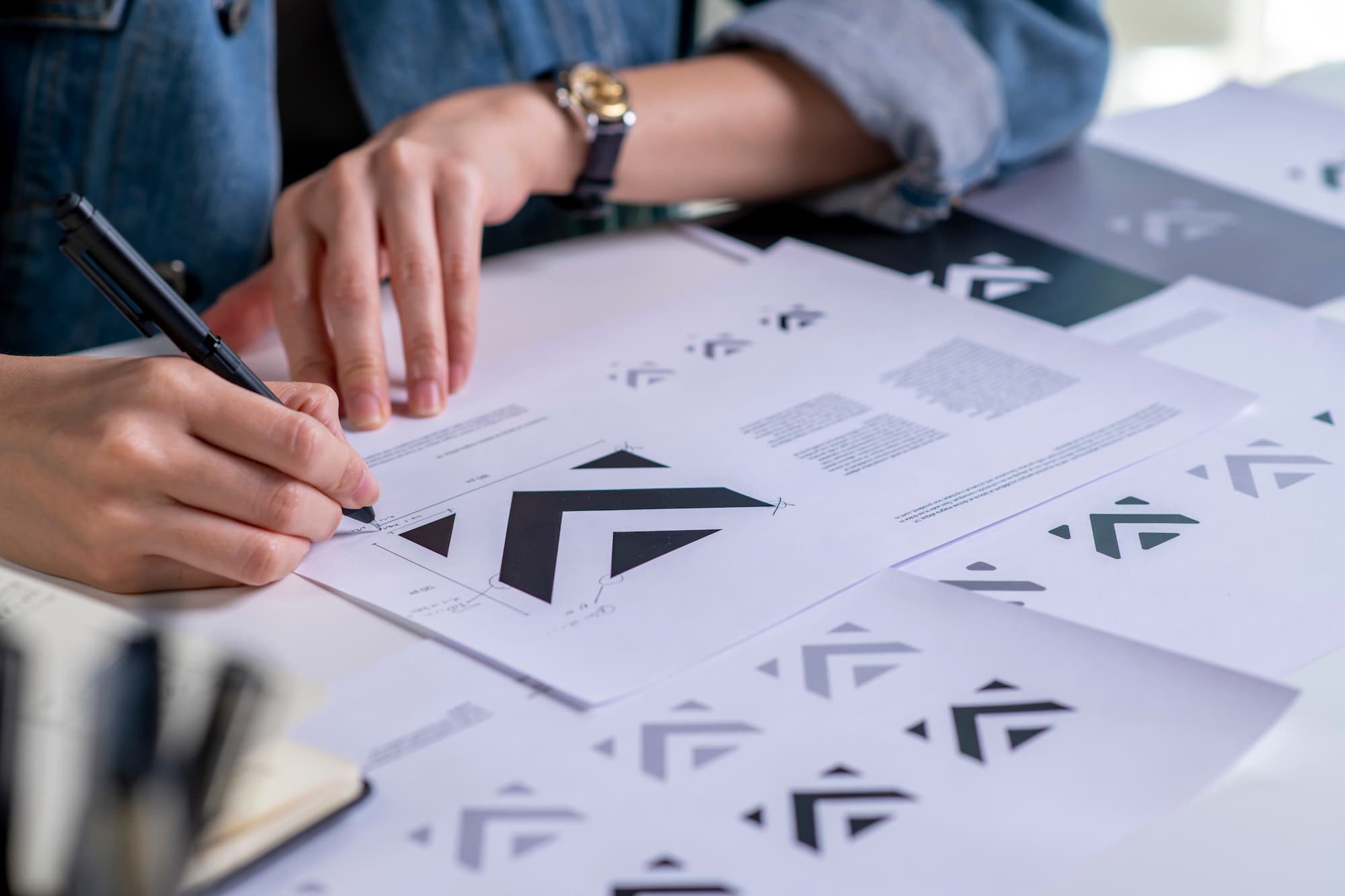 Personne analysant des prototypes de logos avec des formes géométriques sur documents papier