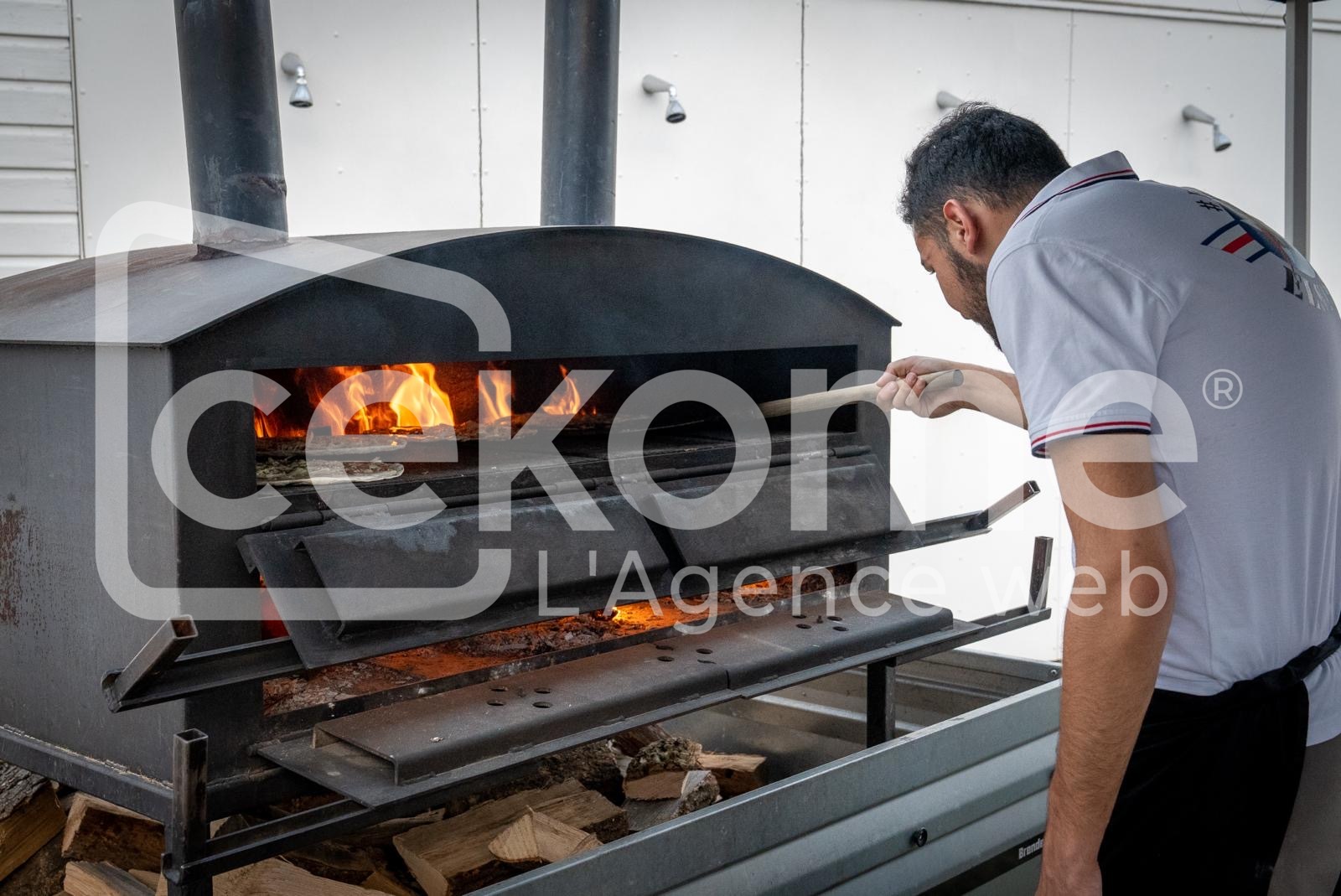 Homme alimentant un four à pizza en plein air lors d'un événement Cekome.