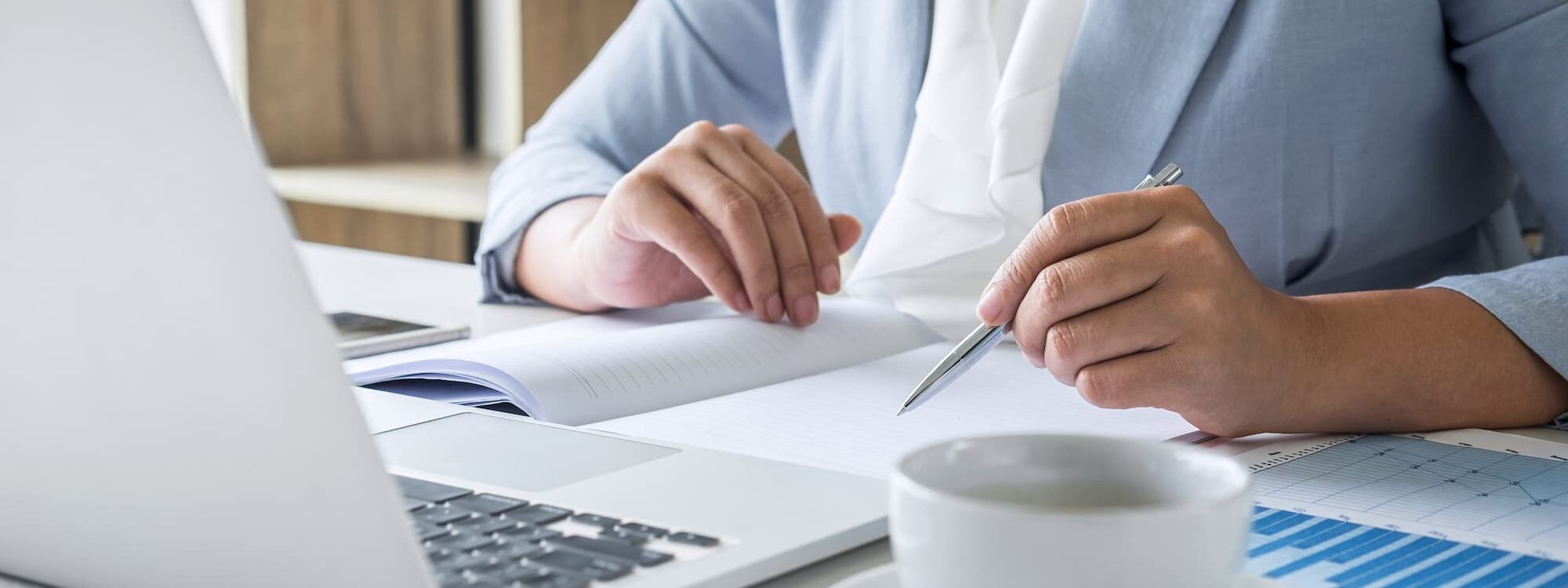 Professionnelle en finance consultant des documents et travaillant sur ordinateur portable avec une tasse de café.