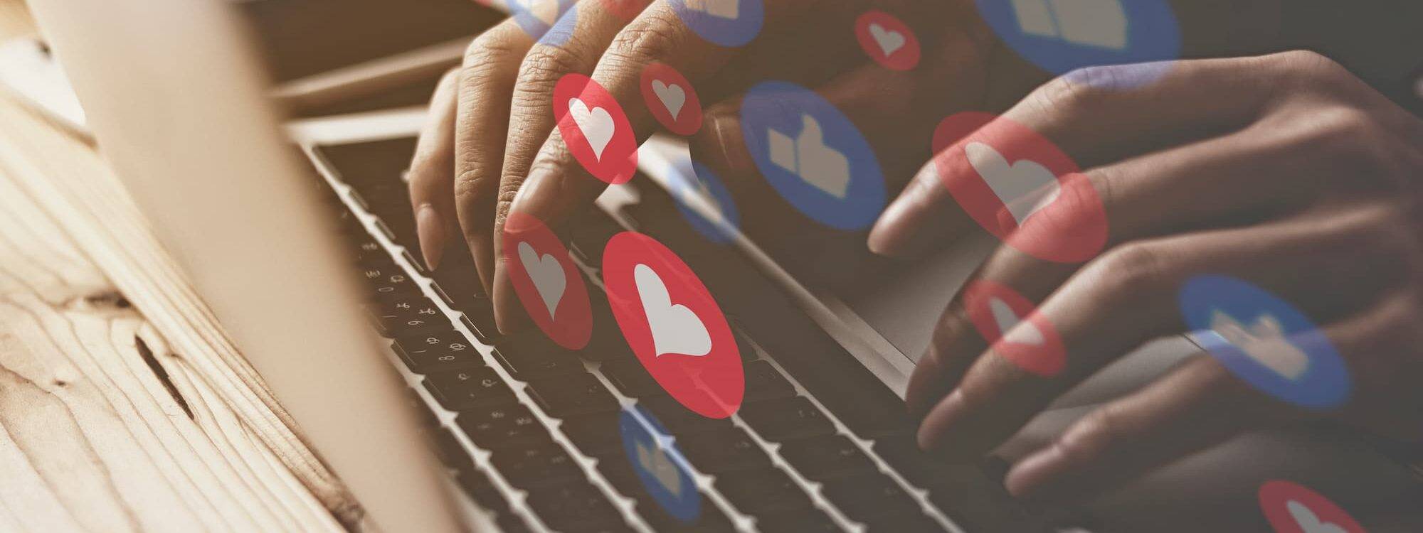 Mains tapant sur un clavier avec des icônes de réactions des réseaux sociaux comme des cœurs et des pouces en l'air.