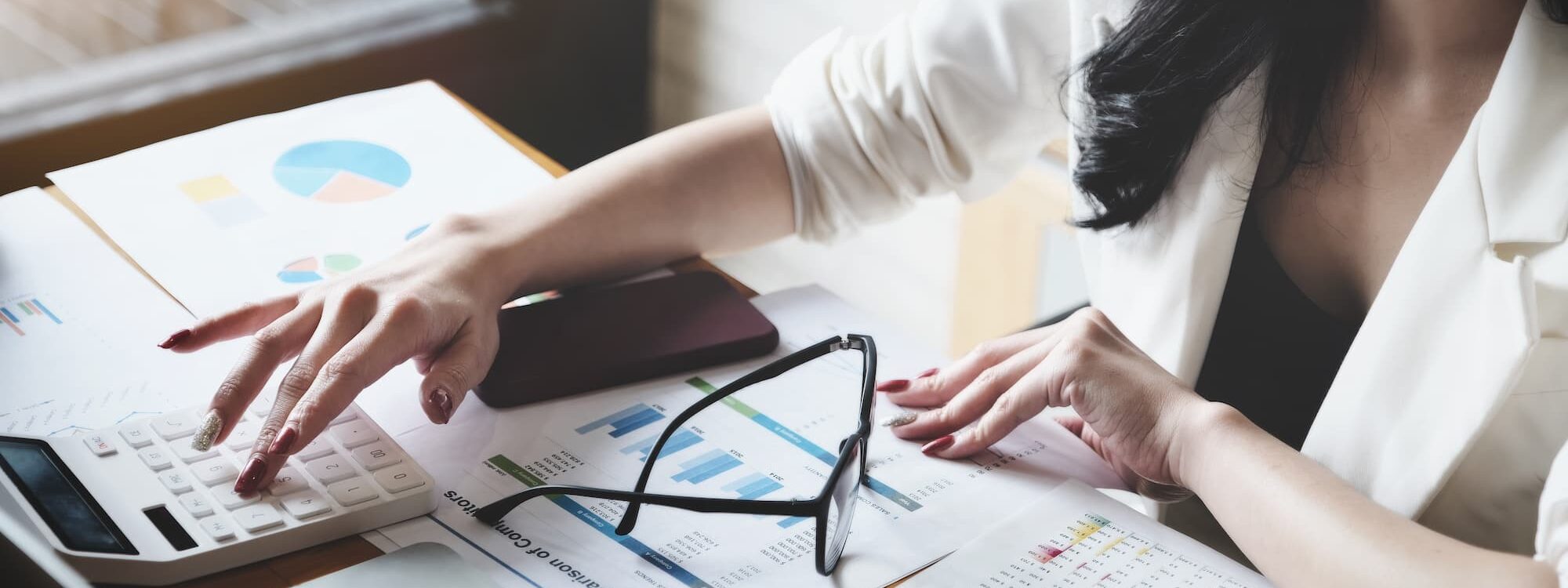 Femme d'affaires calculant des statistiques financières avec des graphiques et un ordinateur portable.