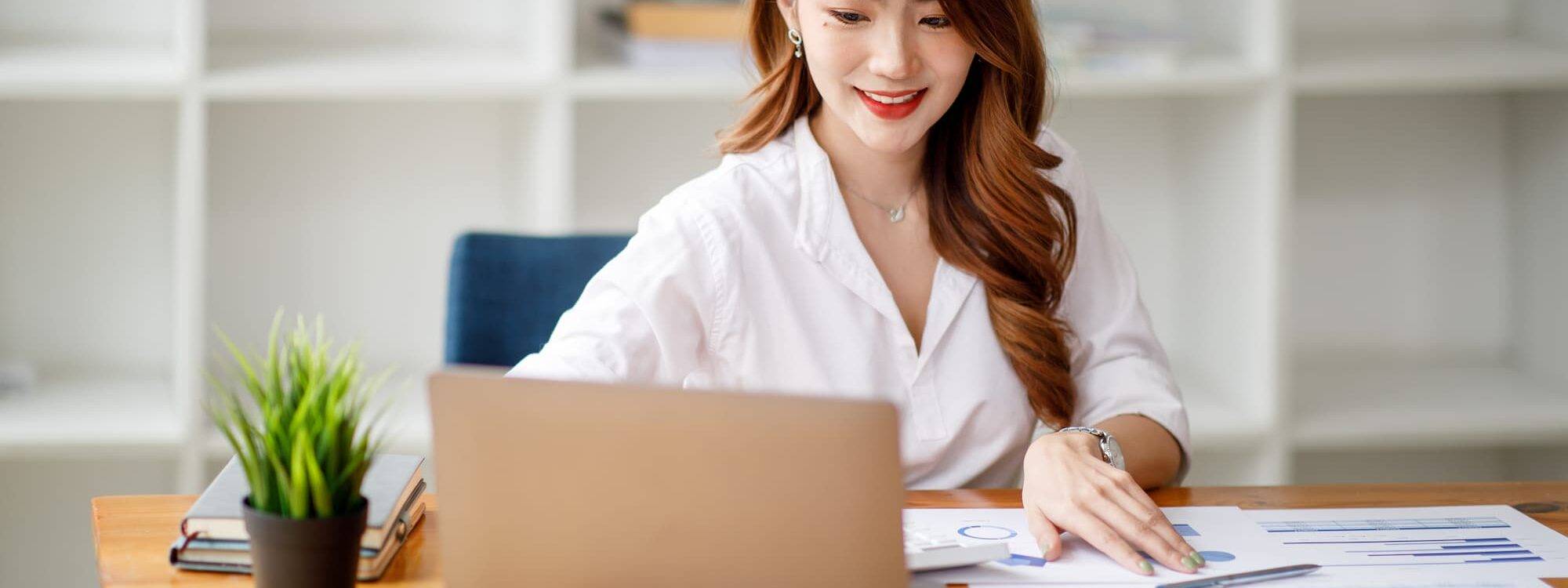 Jeune femme entrepreneur examinant des rapports financiers sur son bureau avec ordinateur portable ouvert.