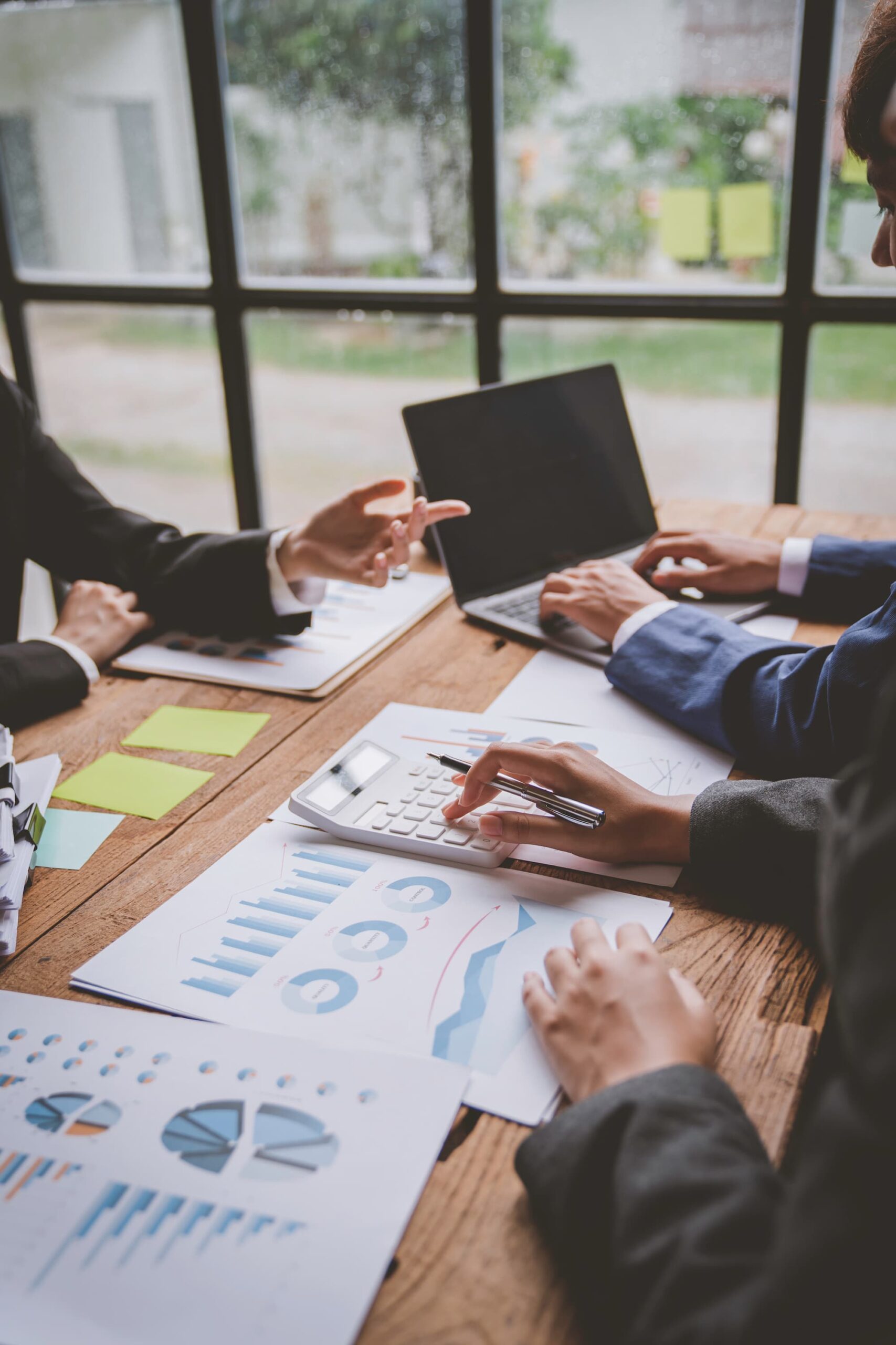 Réunion d'équipe analysant des rapports financiers avec des post-it et un ordinateur portable sur la table.