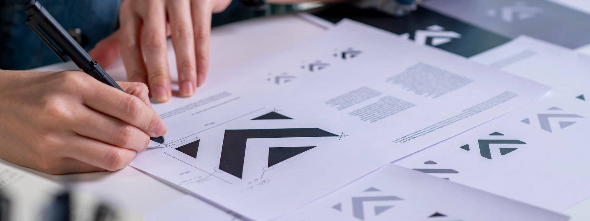 Personne analysant des prototypes de logos avec des formes géométriques sur documents papier