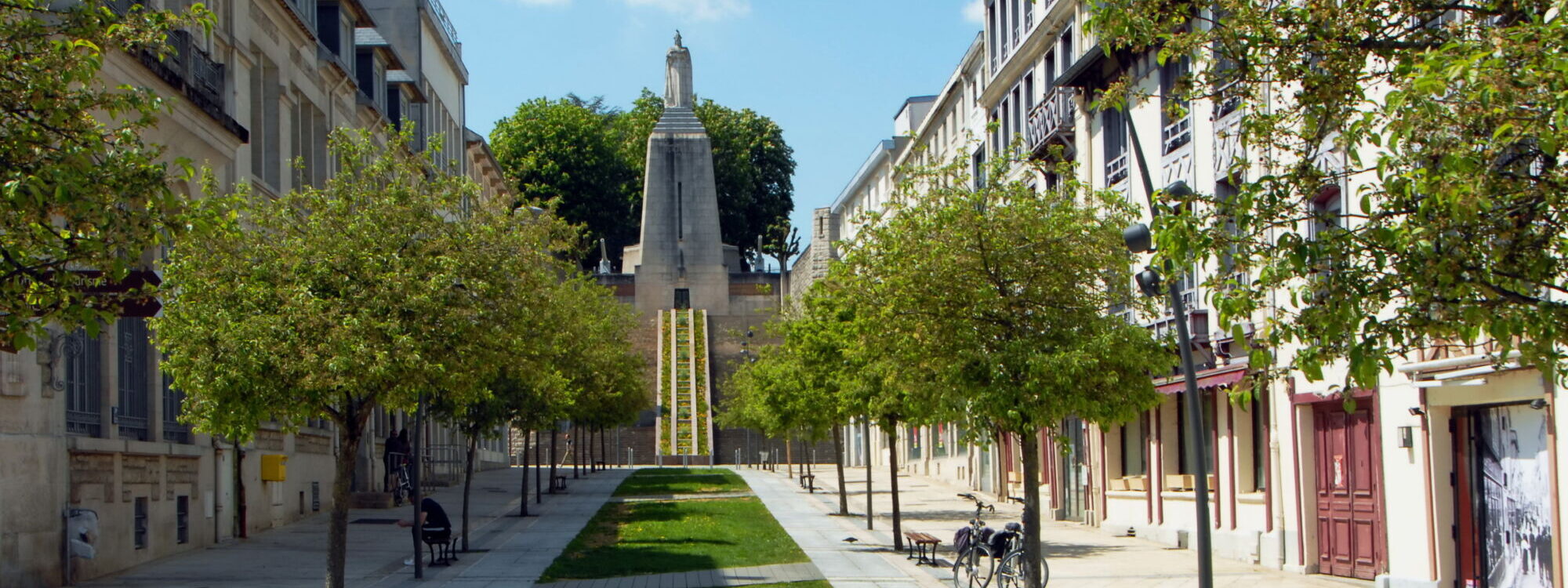 Allée piétonne bordée d'arbres menant à un monument commémoratif en ville.