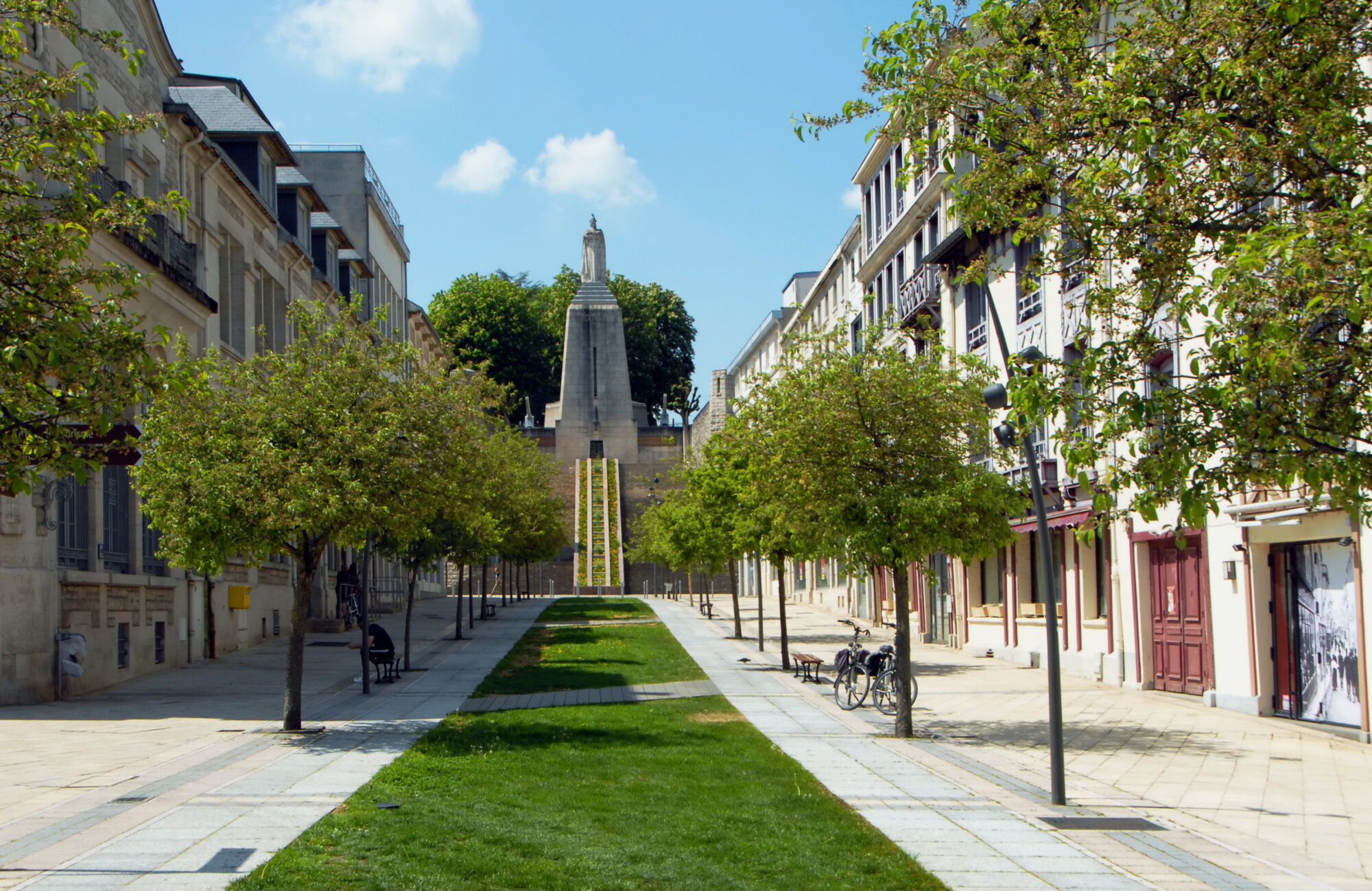 Allée piétonne bordée d'arbres menant à un monument commémoratif en ville.