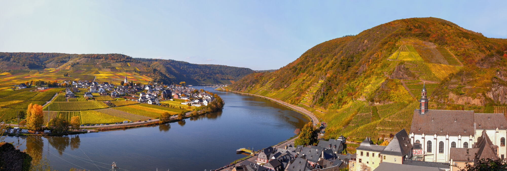 Vue aérienne d'un village bordant une rivière avec des vignobles sur les coteaux.