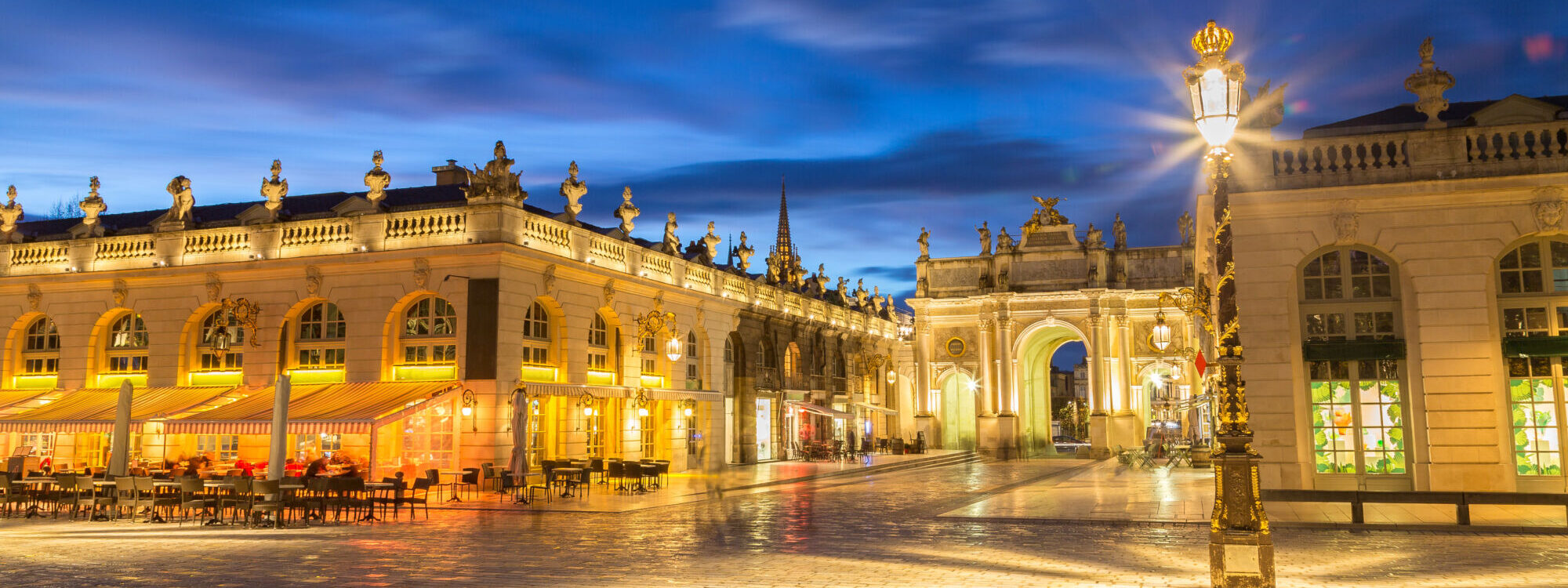 Place royale illuminée la nuit avec architecture classique et ciel nuageux.