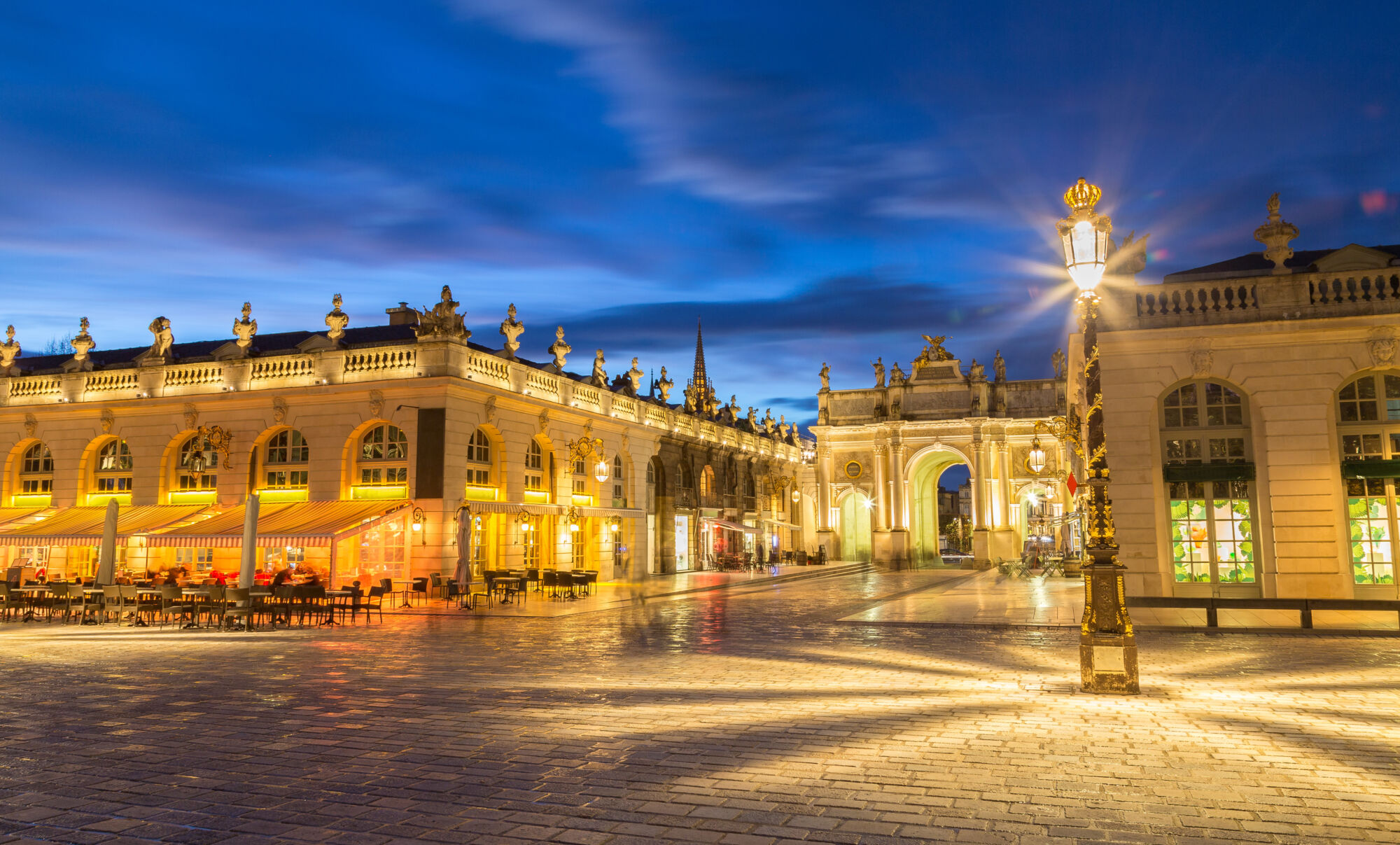 Place royale illuminée la nuit avec architecture classique et ciel nuageux.