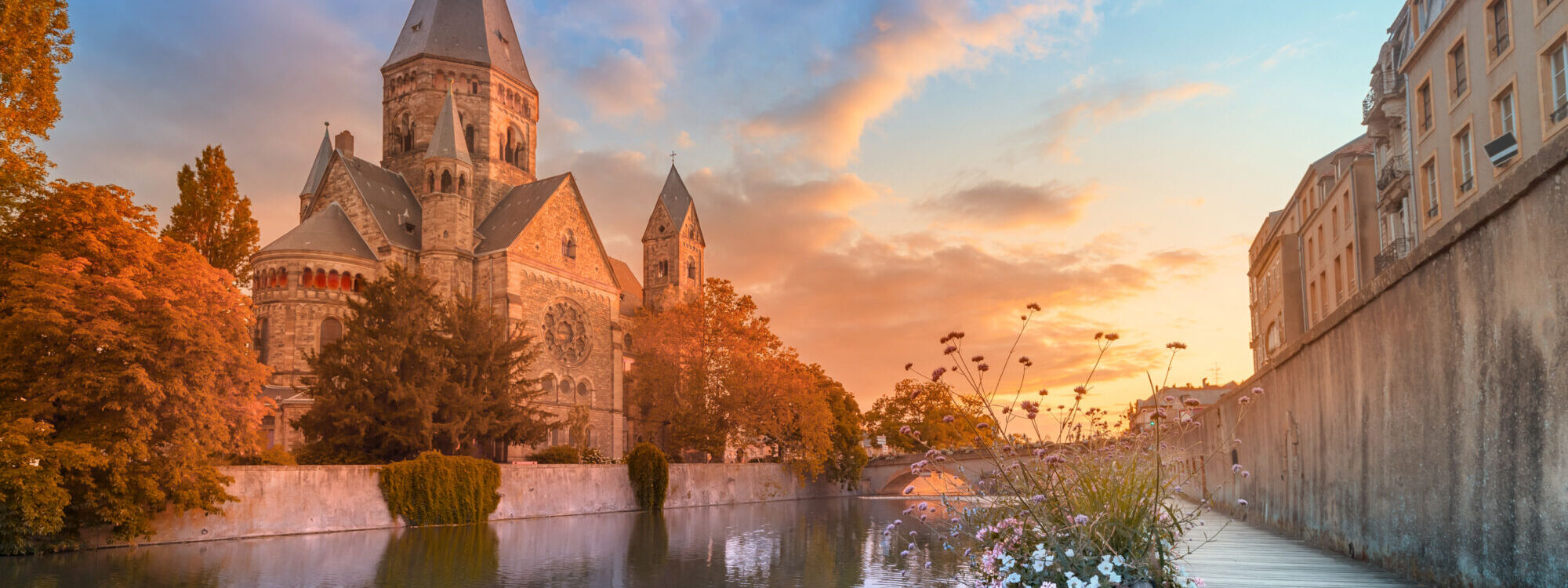 Église romane au bord de l'eau éclairée par un coucher de soleil avec ciel coloré.