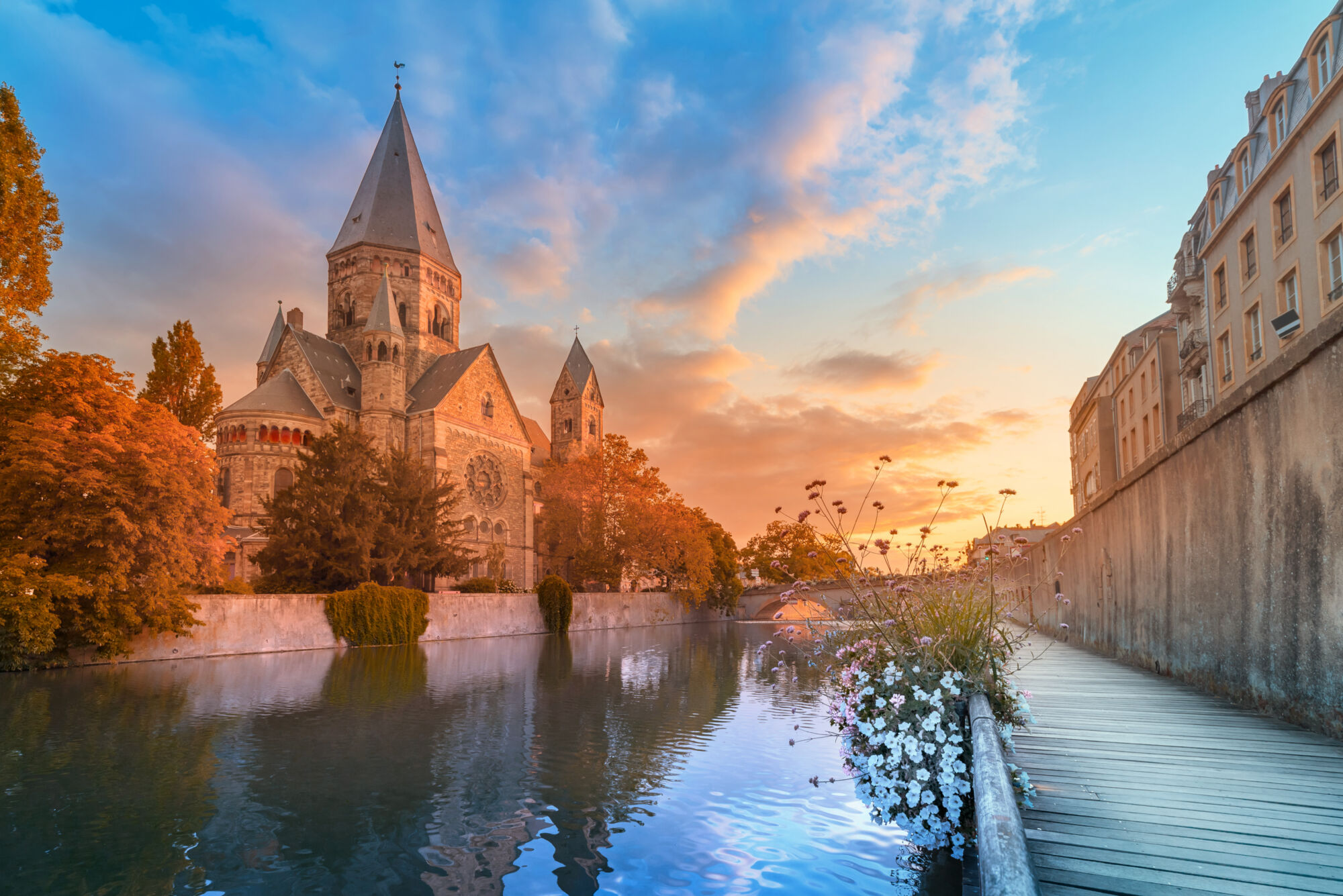 Église romane au bord de l'eau éclairée par un coucher de soleil avec ciel coloré.